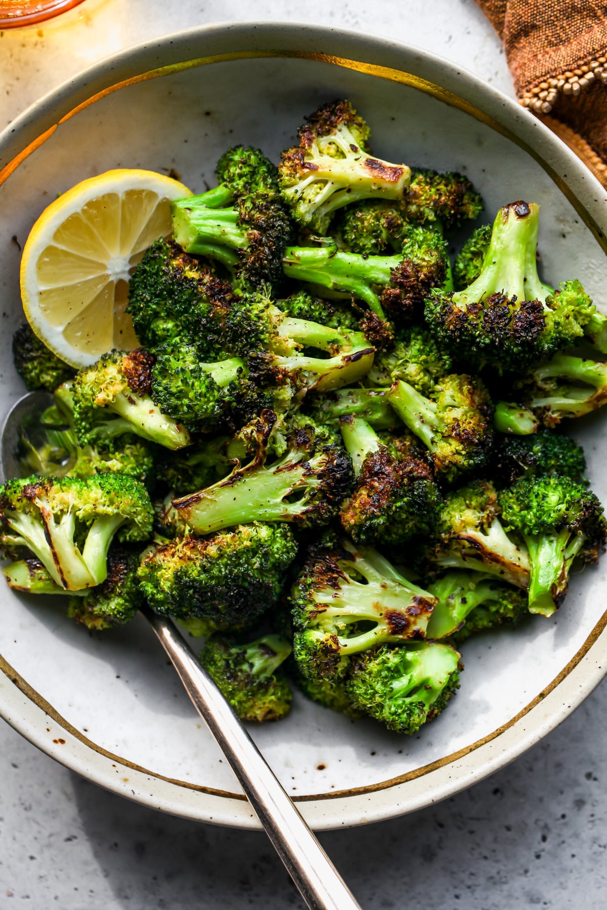 Sautéed broccoli florets in a tan bowl with a spoon resting on the left side.