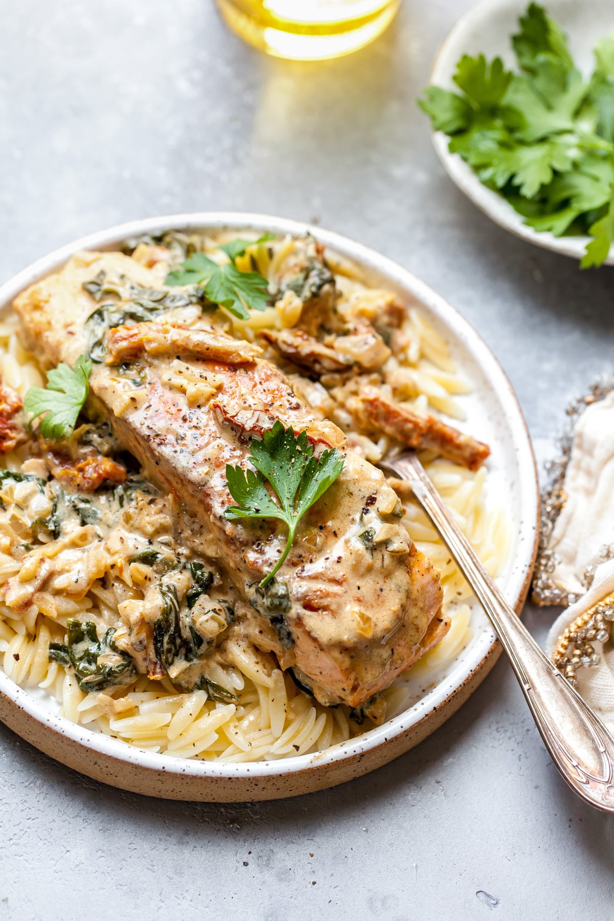 Sun-dried tomato salmon fillet on a bed of orzo pasta on a small white plate.