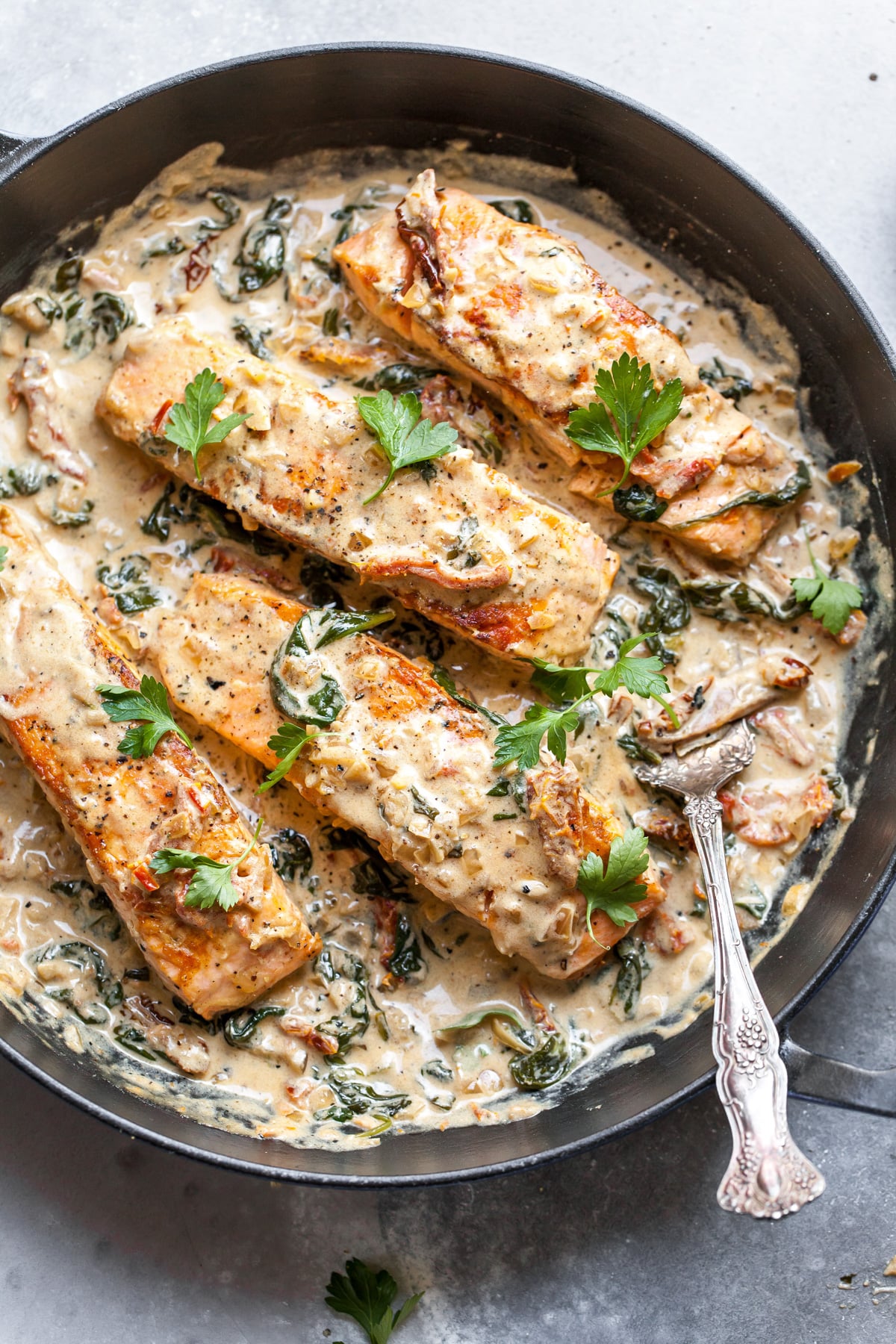 Salmon fillets in a sun-dried tomato cream sauce in a black pan.