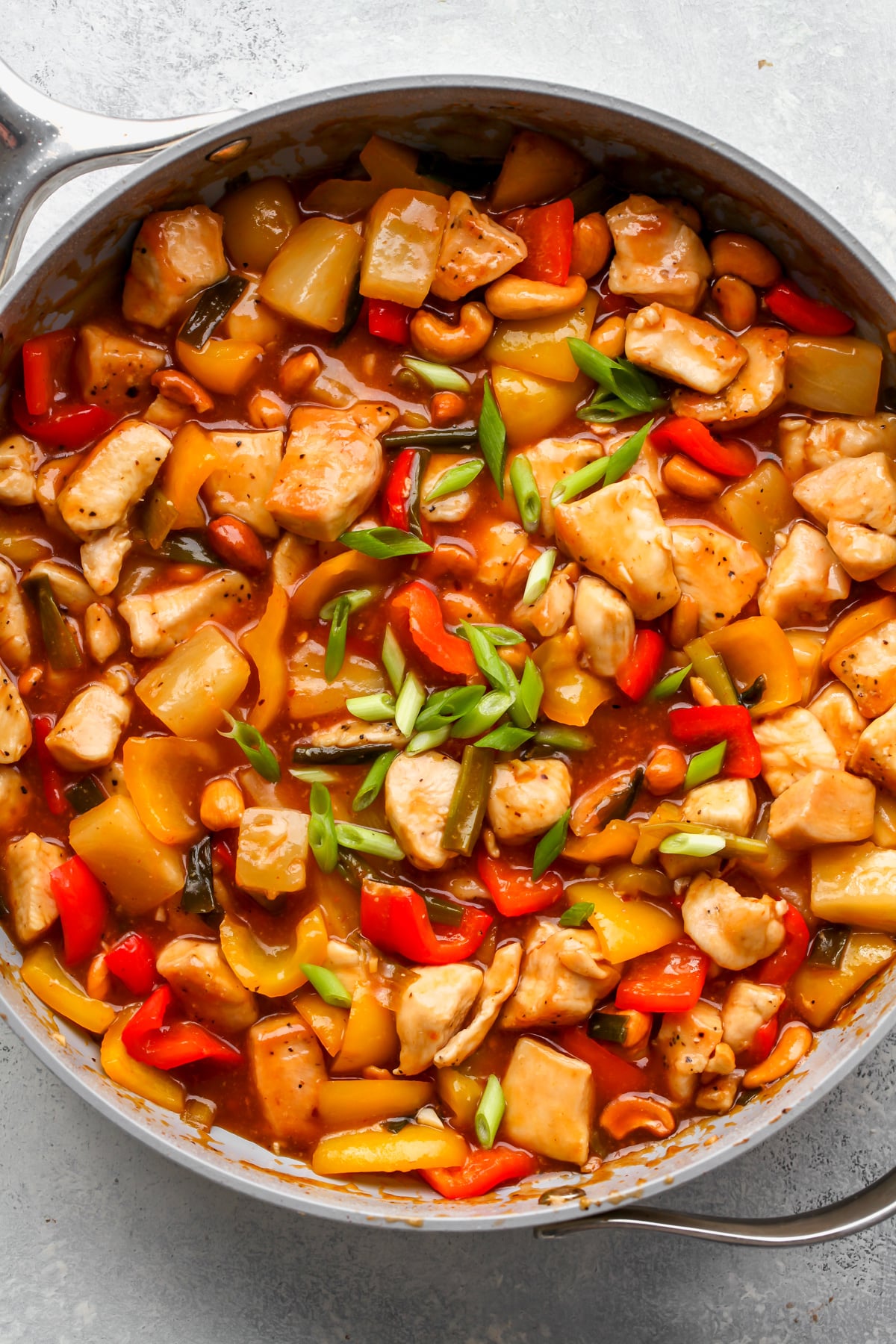 Sweet and sour chicken simmering in sauce in a large skillet. Topped with sliced green onion.