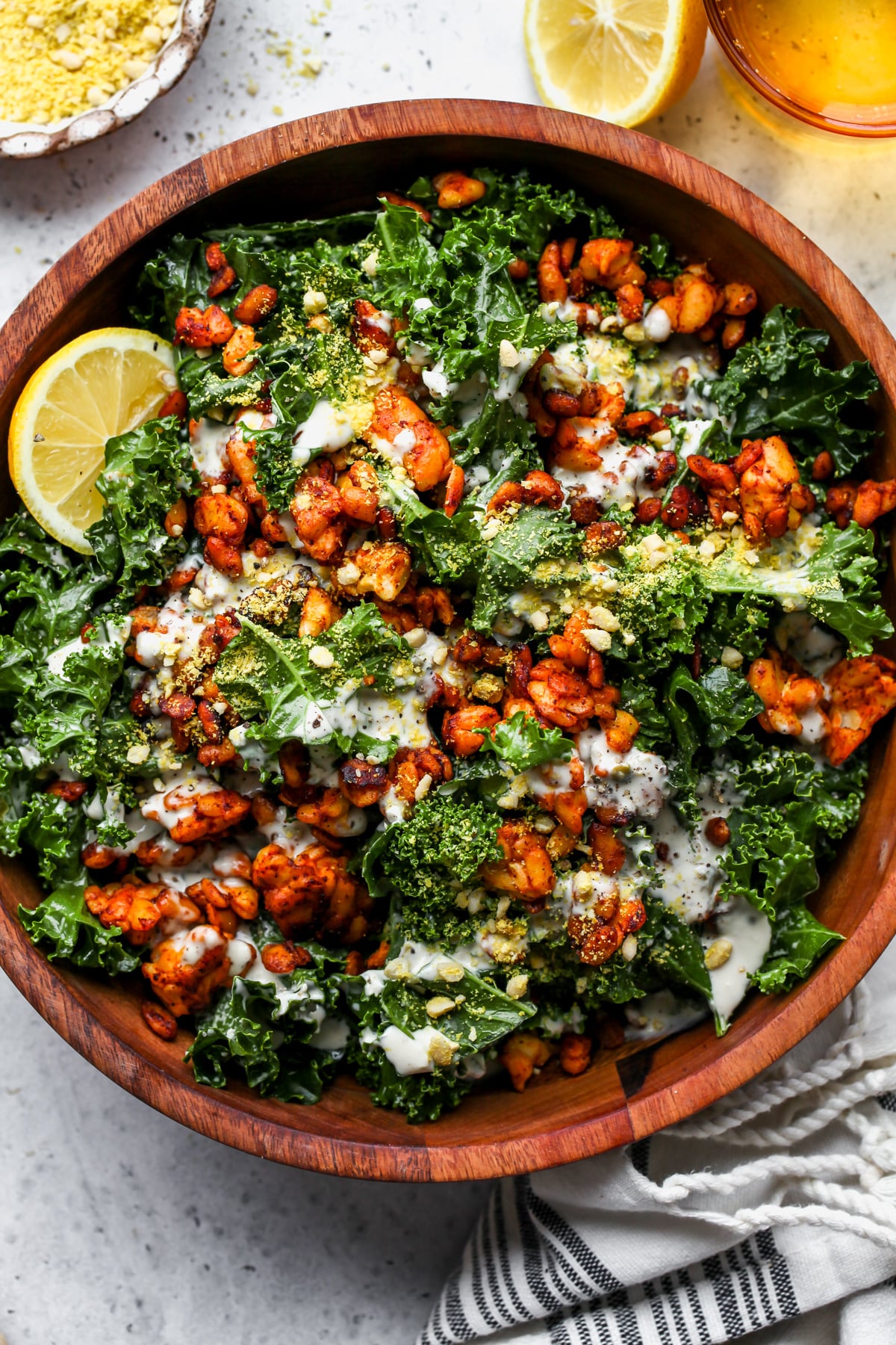 Vegan kale caesar topped with smokey tempeh crumbles in a wooden salad bowl.