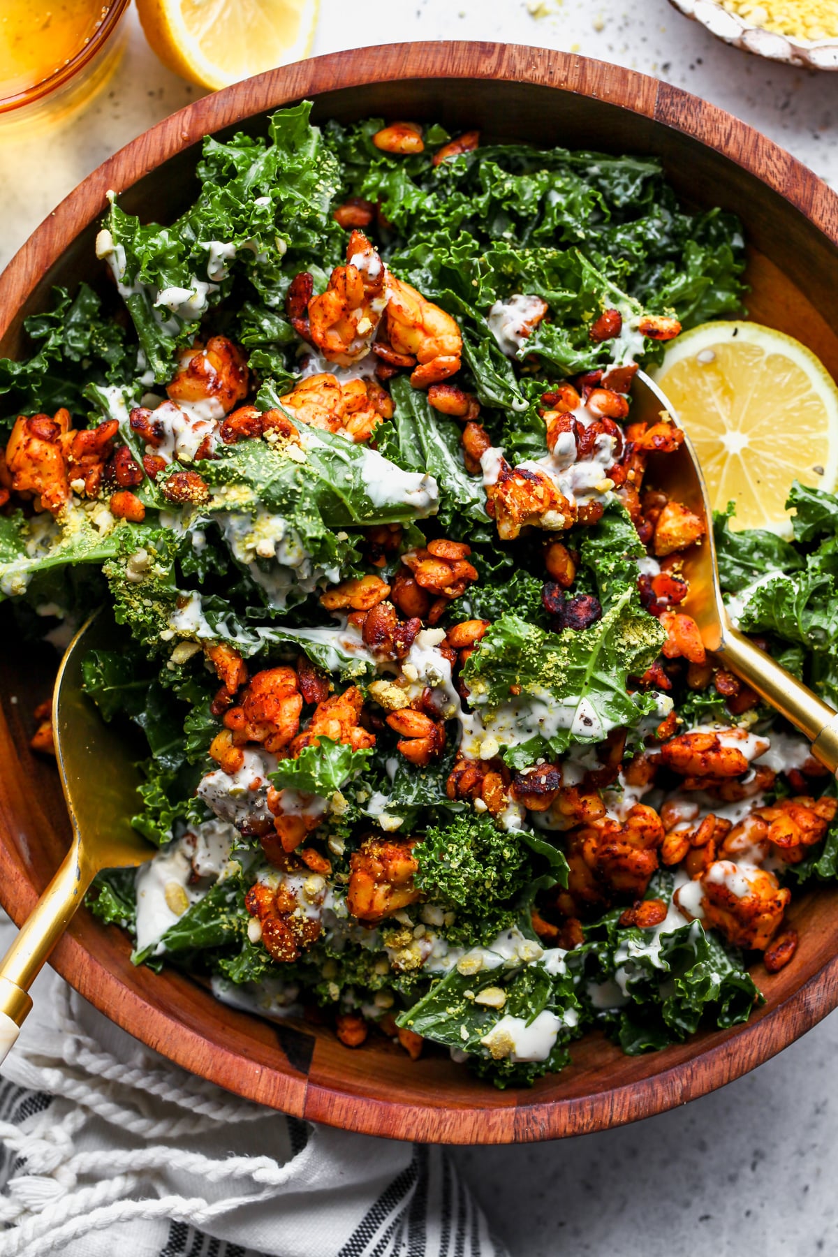 Vegan Kale Caesar Salad with tempeh crumbles being tossed with gold salad tongs in a wooden bowl.