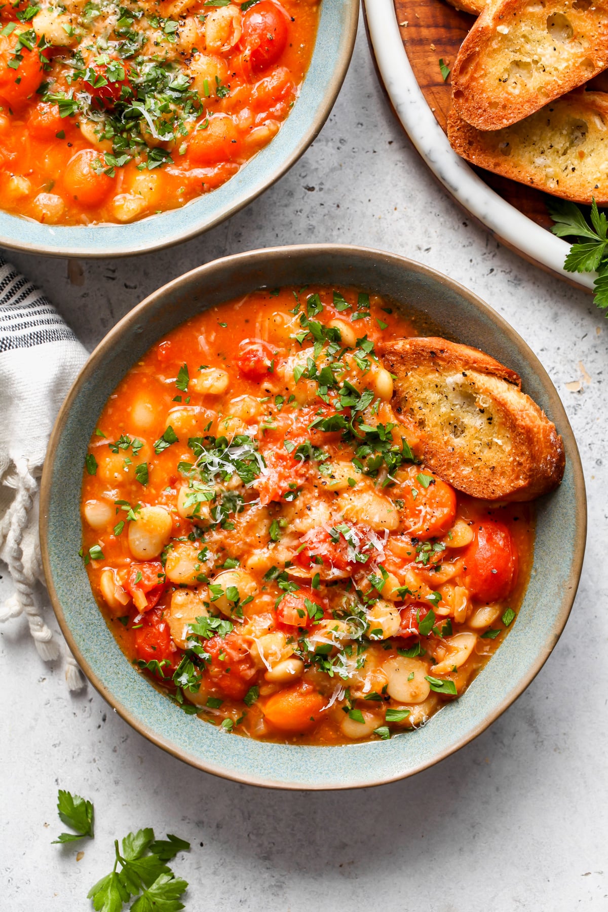 Tomato and butter bean stew styled in a blue bowl topped with parsley and Parmesan.