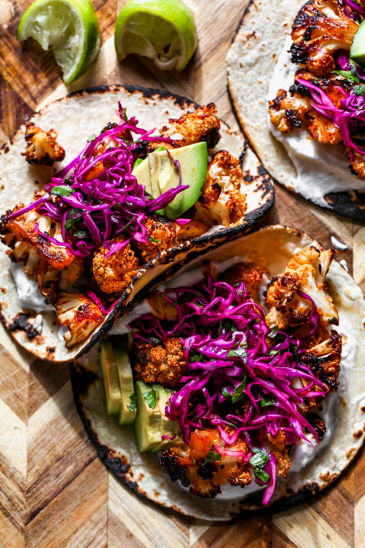 Chipotle cauliflower tacos arranged on a cutting board, surrounded by lime wedges.