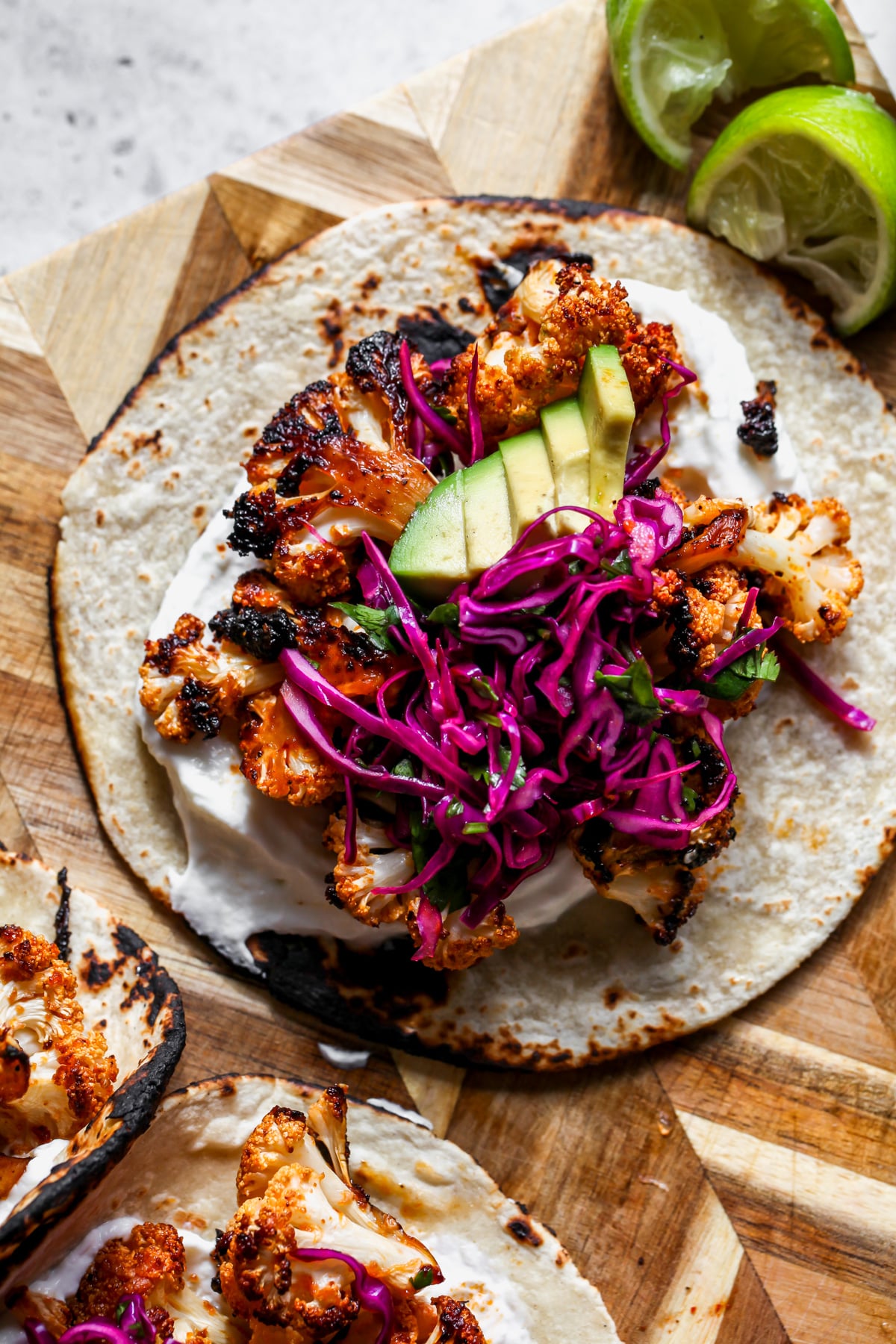 Chipotle cauliflower tacos topped with a cabbage slaw styled on a wooden cutting board.