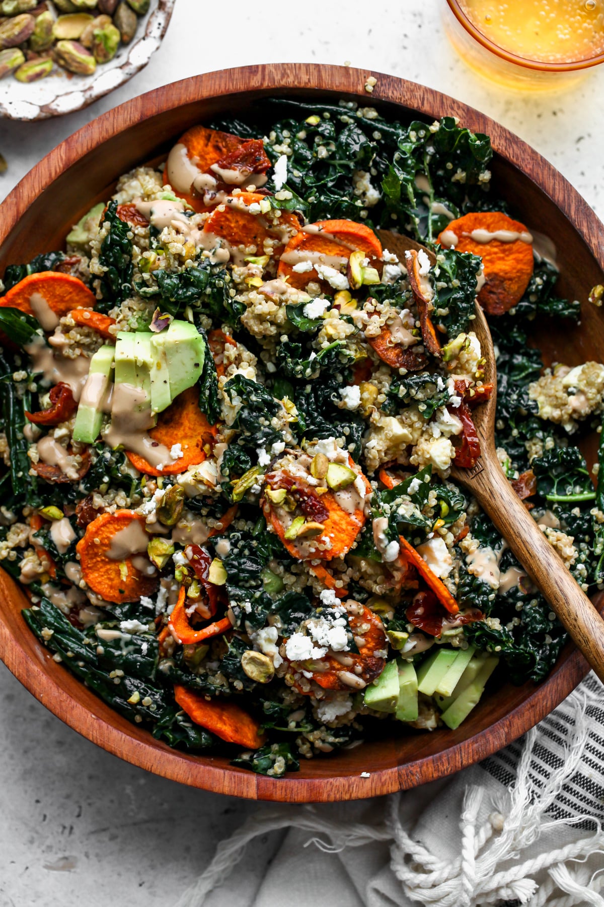 Kale and sweet potato salad being tossed with wooden salad spoons in a wooden serving bowl.