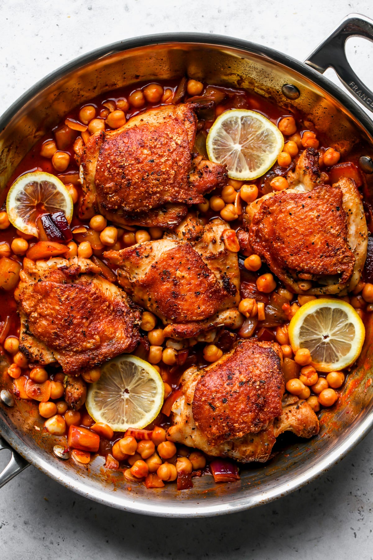 Chicken thighs nestled in a pan of chickpeas with lemon slices arranged around the chicken.