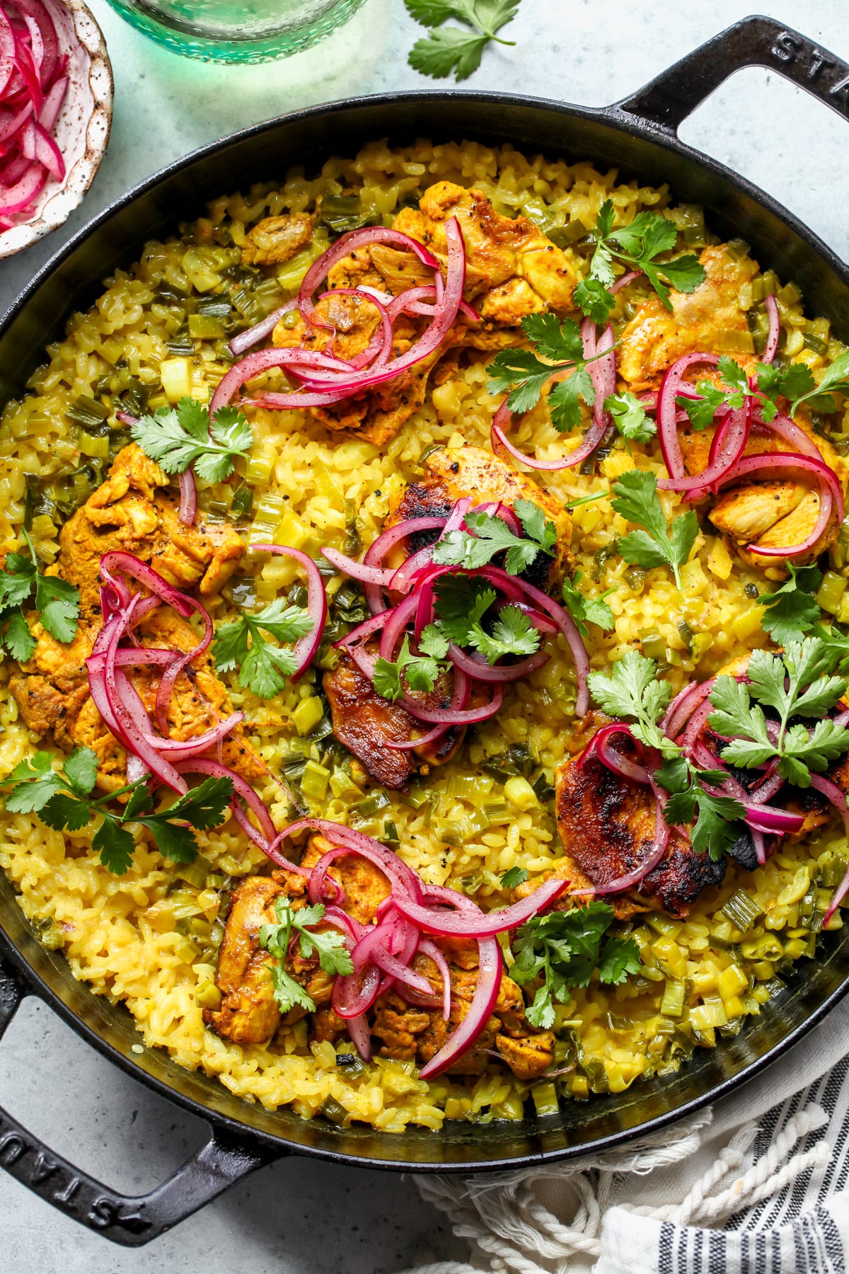 Turmeric chicken and rice in a black cast iron skillet topped with red onion and cilantro.