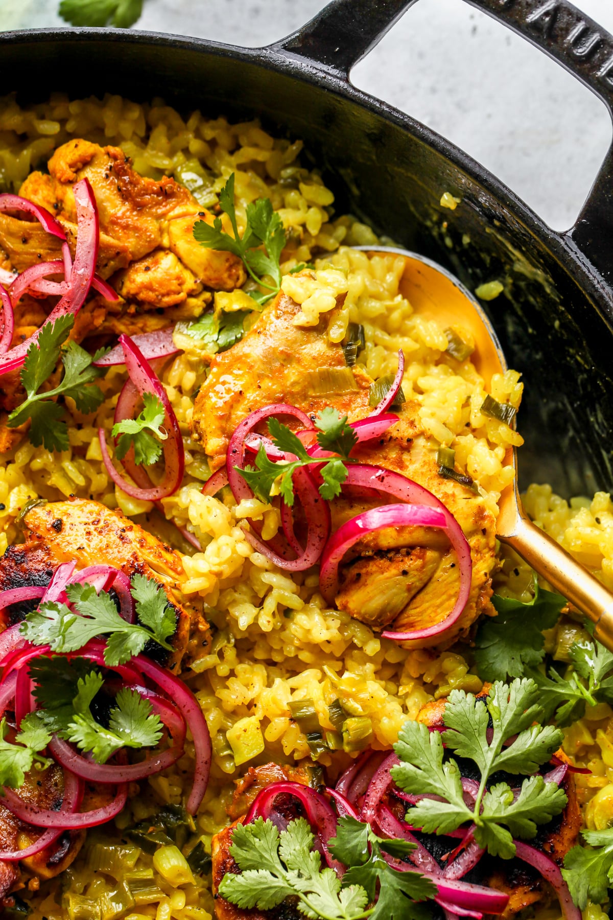 A gold serving spoon digging into a skillet of turmeric chicken and rice.