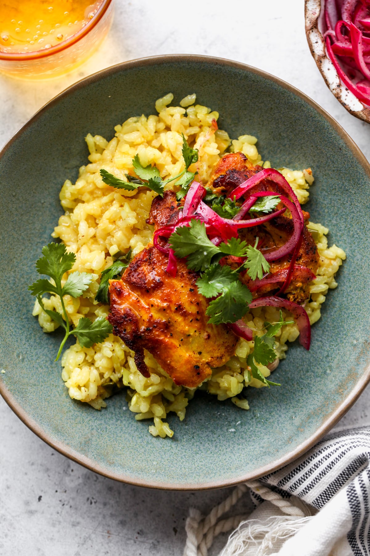 A teal plate filled with a single portion of turmeric chicken and rice, topped with pickled red onion and cilantro.