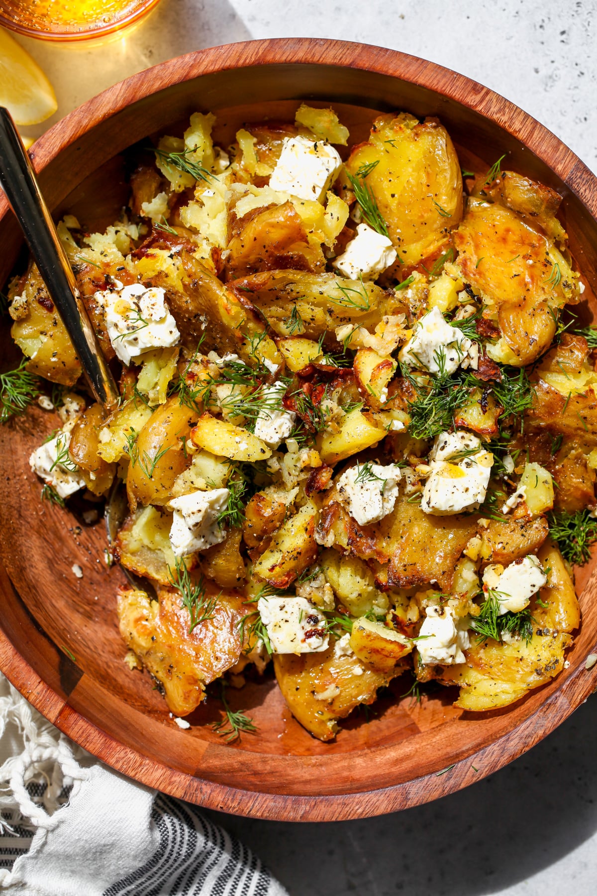 Lemon-feta potatoes being tossed with fresh dill in a wooden bowl.