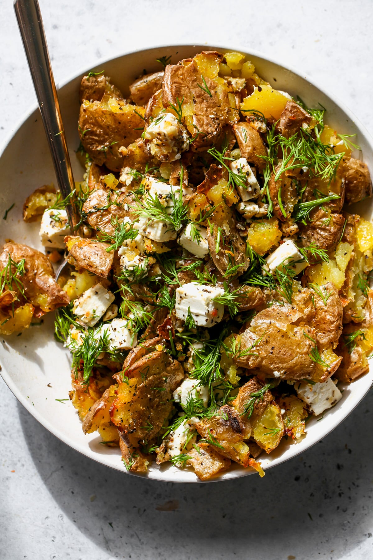 Crispy lemon-feta potatoes will fresh dill styled in a white bowl.