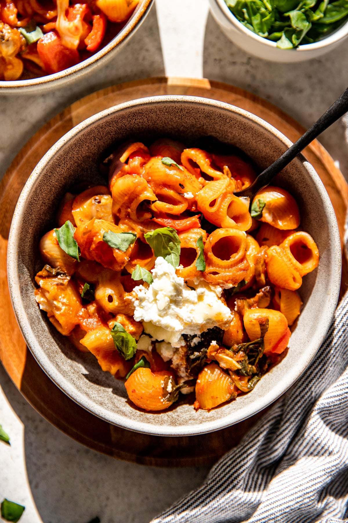 A bowl of vegetable pasta with a fork resting on the right side.