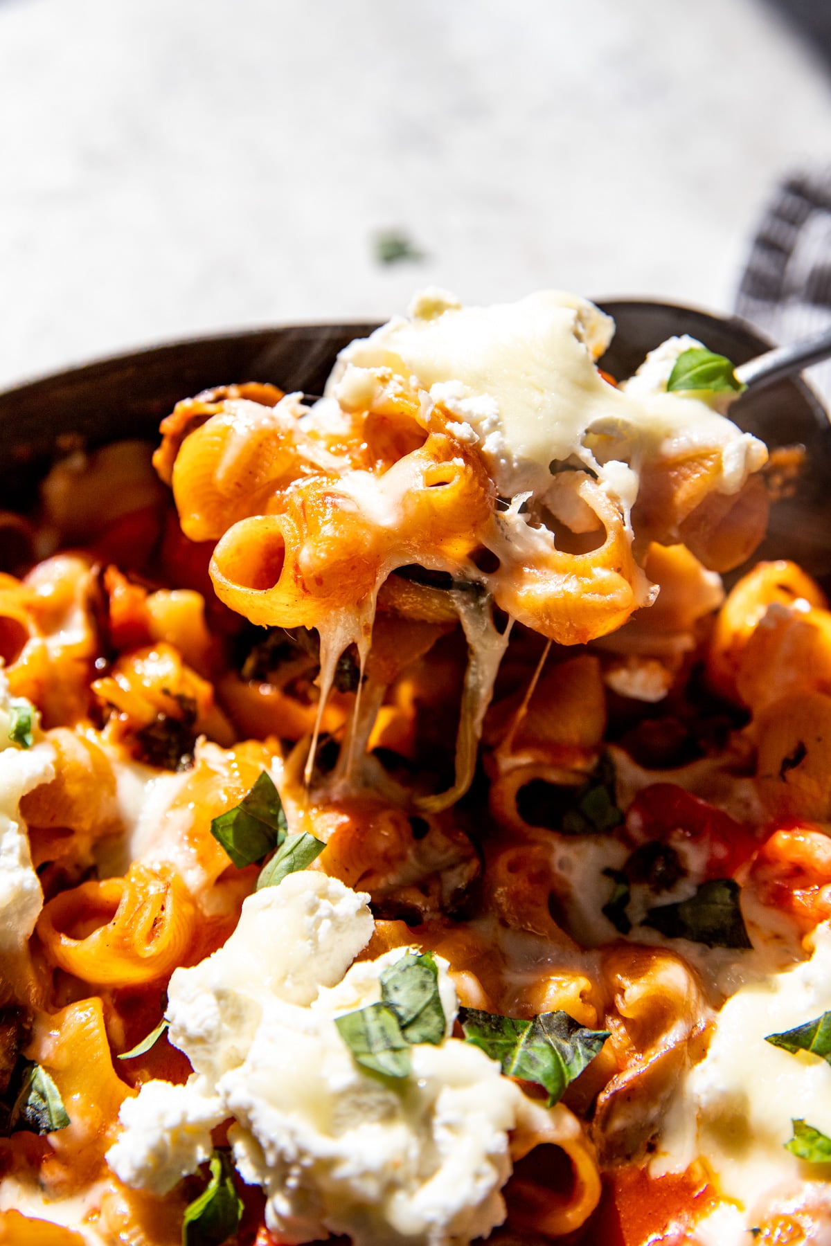 A spoon pulling out a portion of cheesy vegetable pasta bake to show cheese pull.