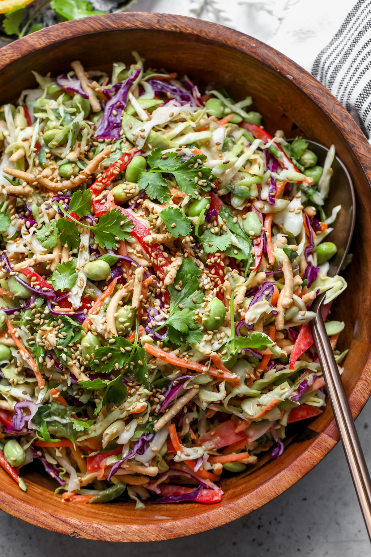 Chopped asian salad styled in a large wooden salad bowl. Garnished with cilantro and sesame seeds.