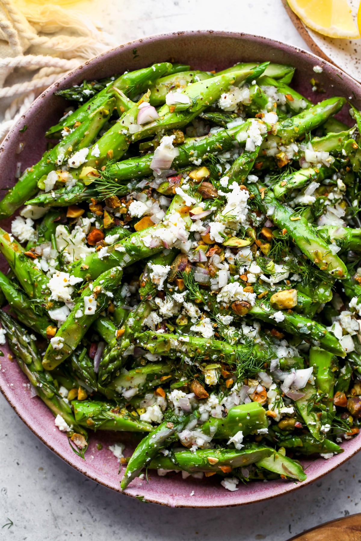 Asparagus and feta salad being mixed in a pink salad bowl.