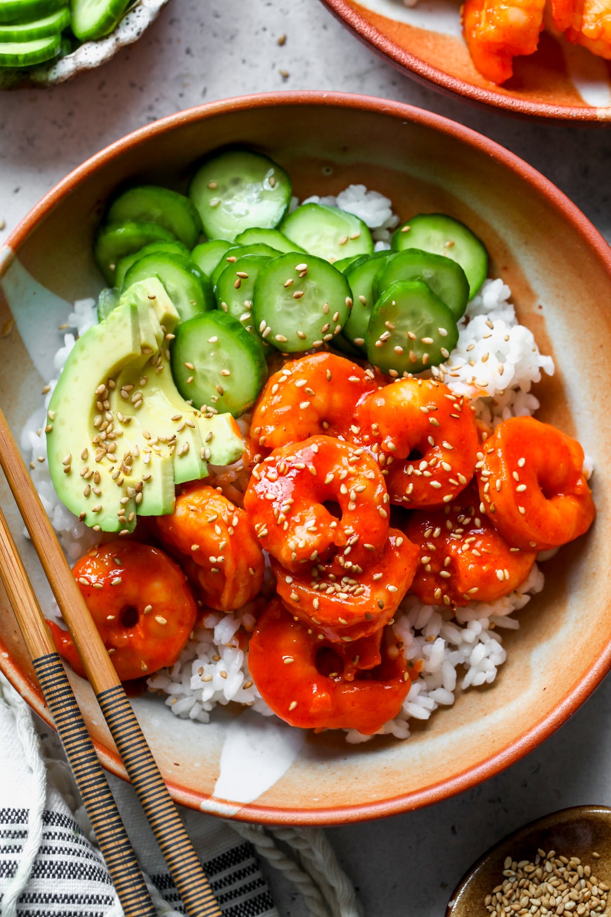 Honey-gochujang shrimp bowls with cucumber and avocado styled in orange bowls.