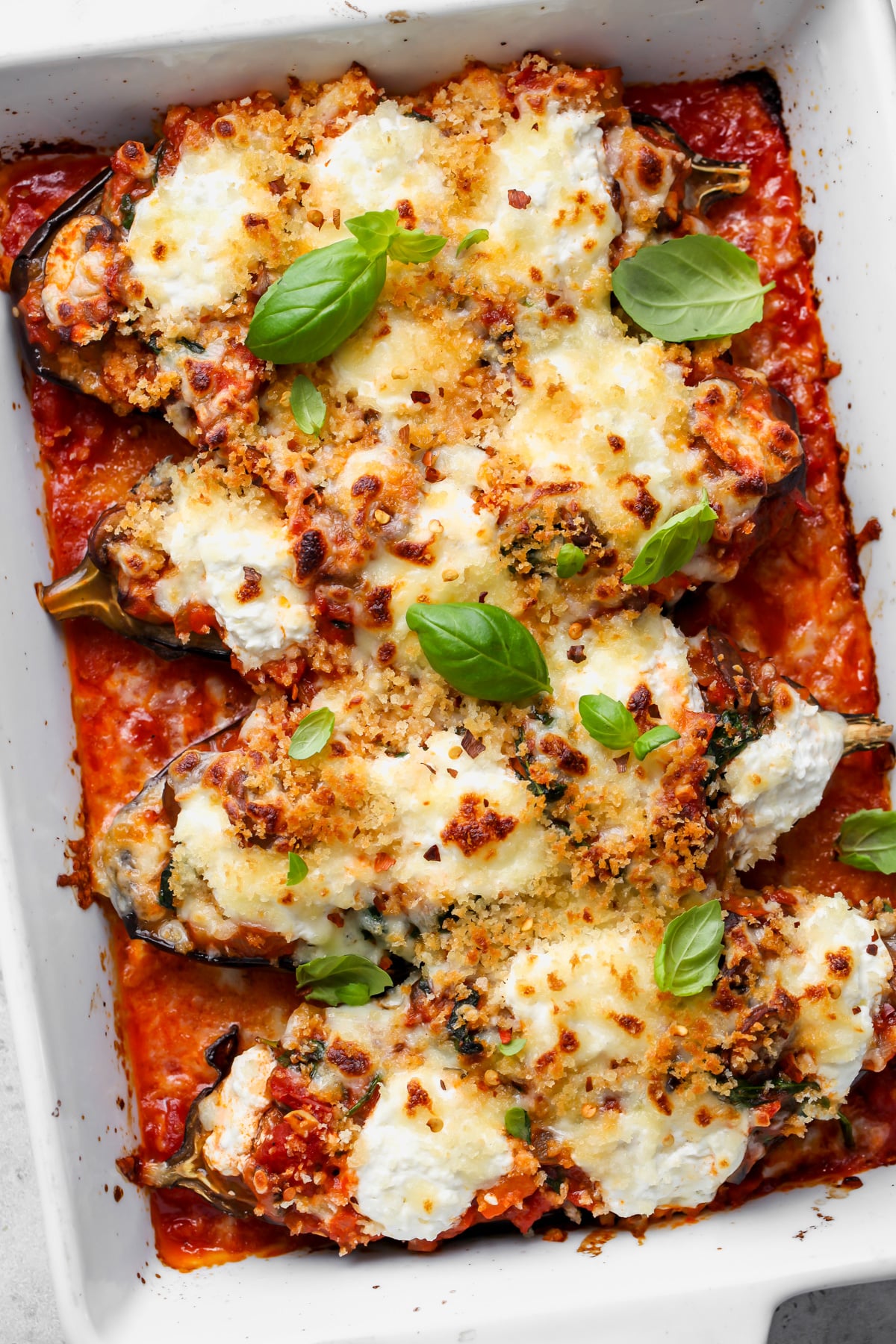 Eggplant lasagna boats arranged in a white baking dish topped with fresh basil leaves.