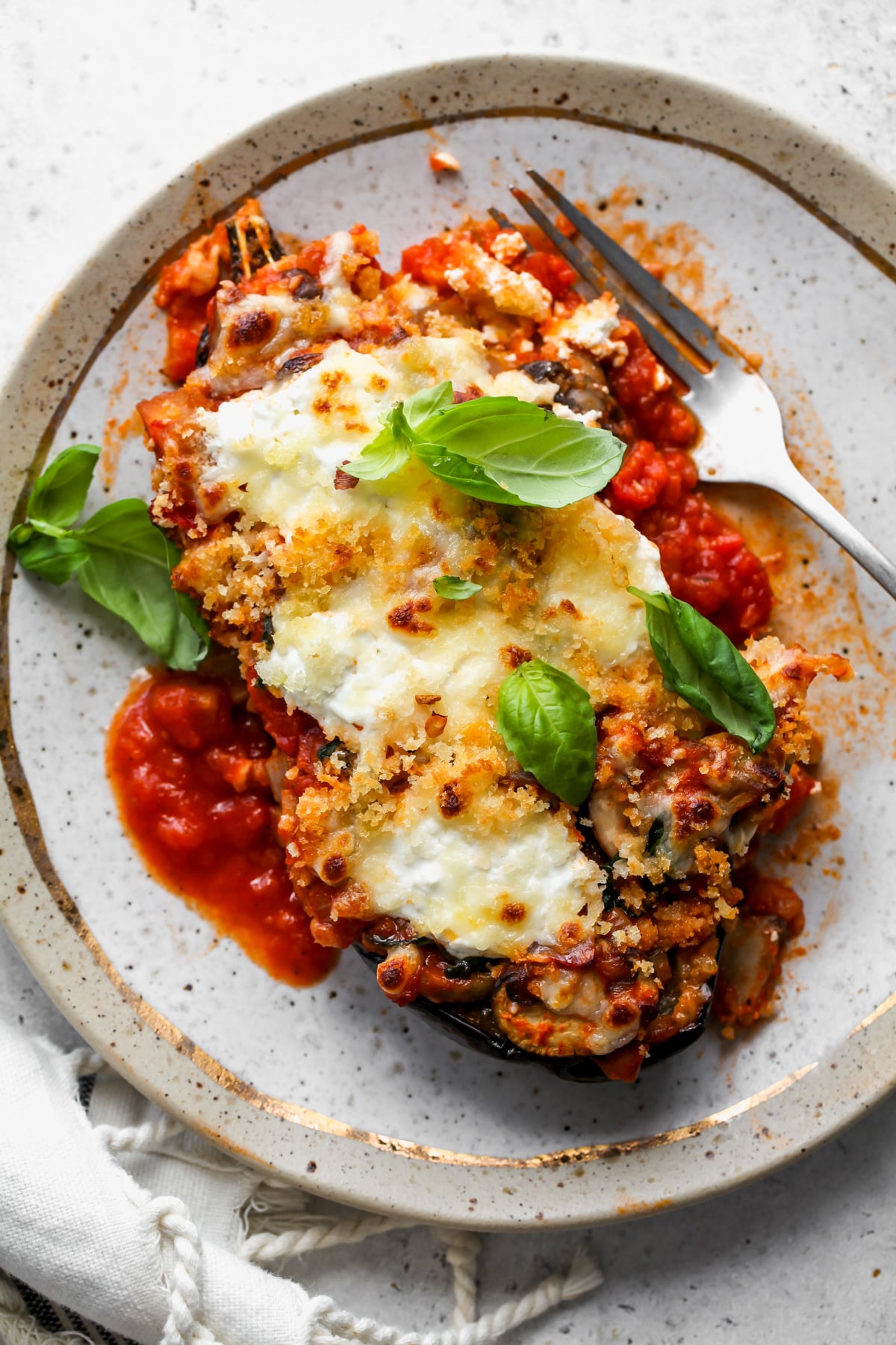 A single stuffed eggplant boat on a white plate topped with fresh basil leaves.