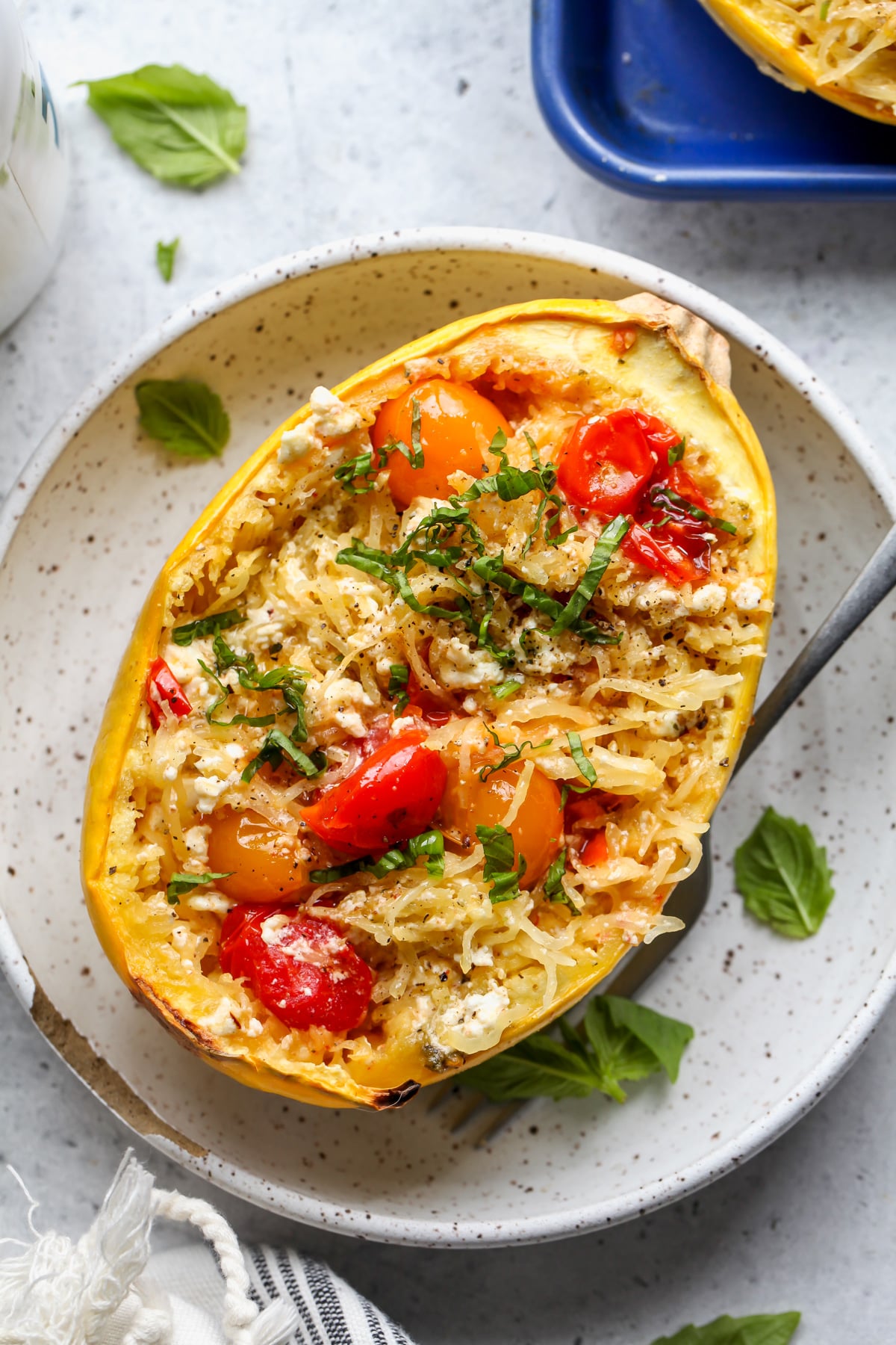 Baked feta spaghetti squash boat styled on a white speckled plate.