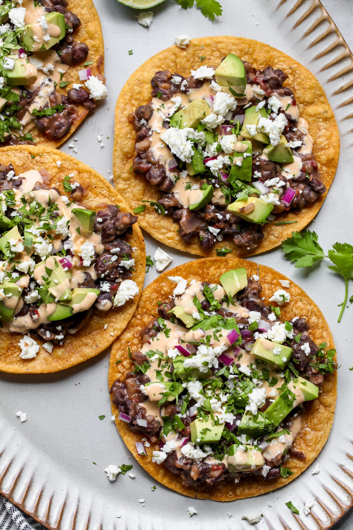 Four black bean tostadas styled on a light blue serving platter.