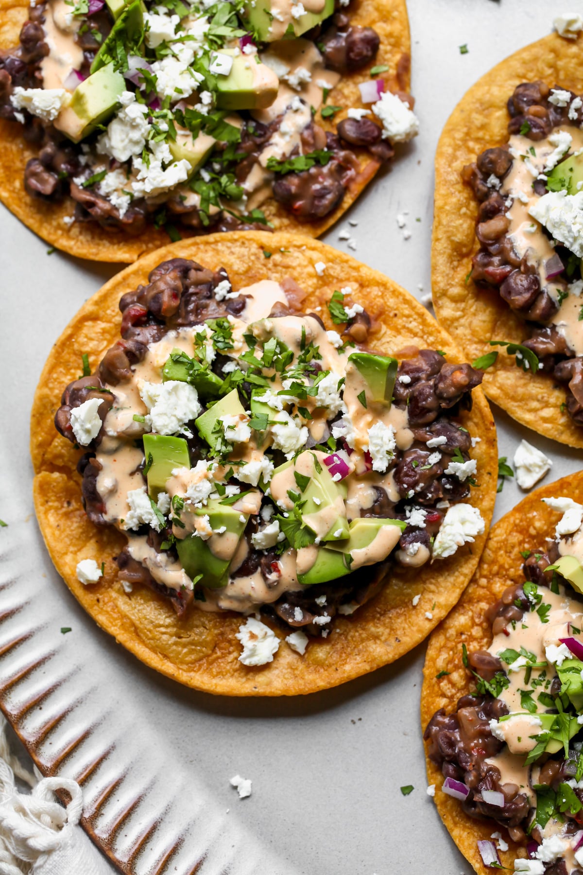 Black bean tostada topped with avocado, cilantro, and jalapeño-sauce sauce on a platter.