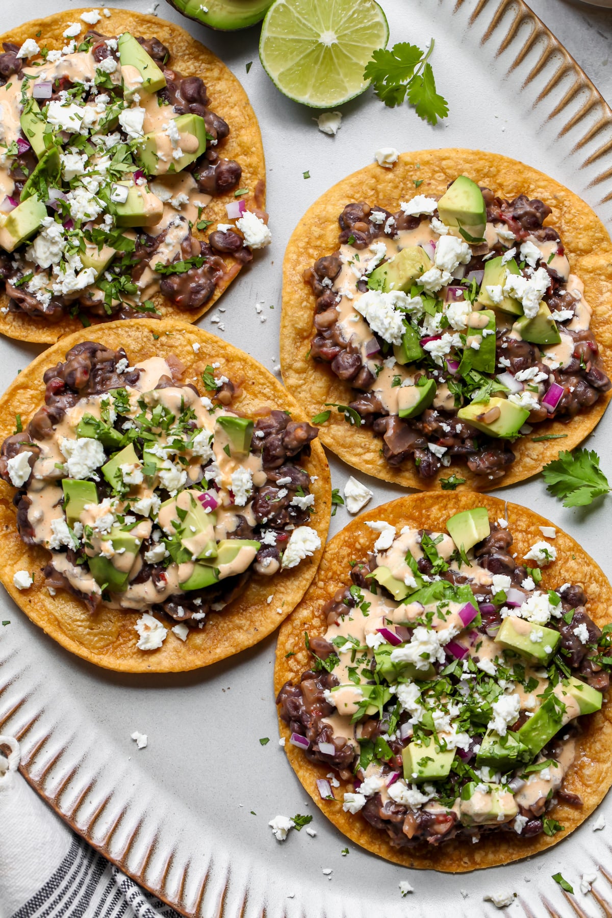 A large serving platter with four styled black bean tostadas arranged with wedges of lime.