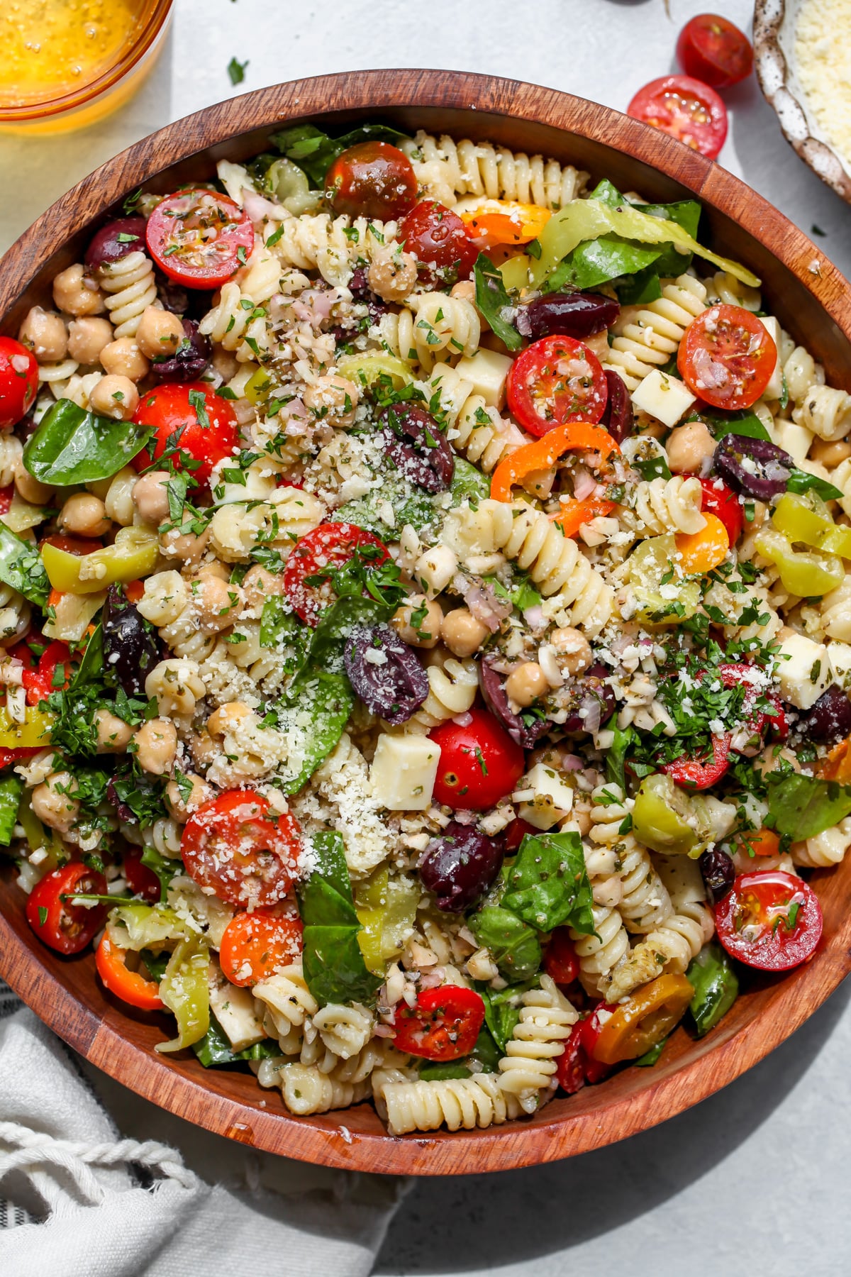A large wooden salad bowl filled with vegetarian Italian pasta salad. Garnished with Parmesan and dried herbs.