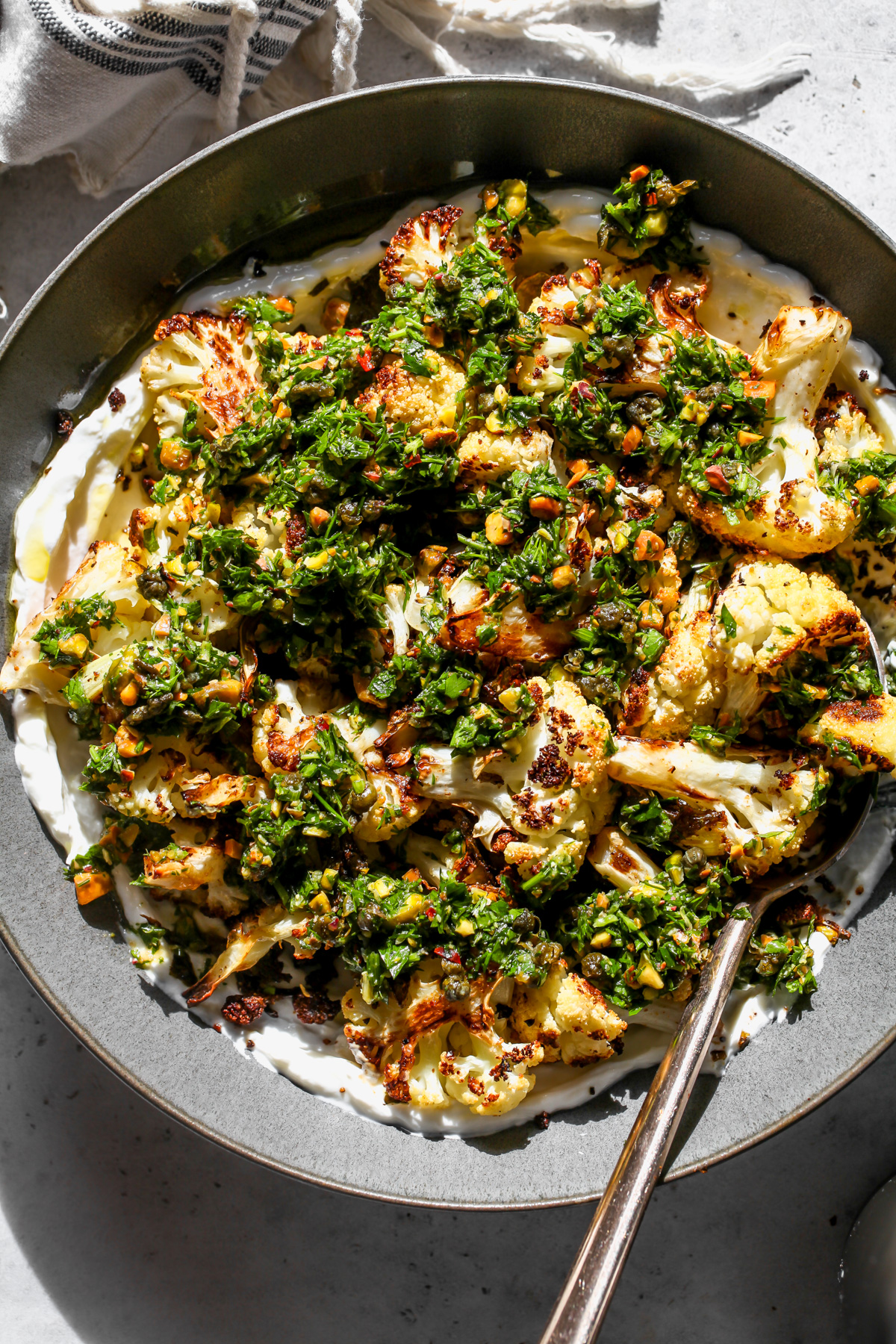Cauliflower with caper gremolata served over yogurt in a gray bowl.