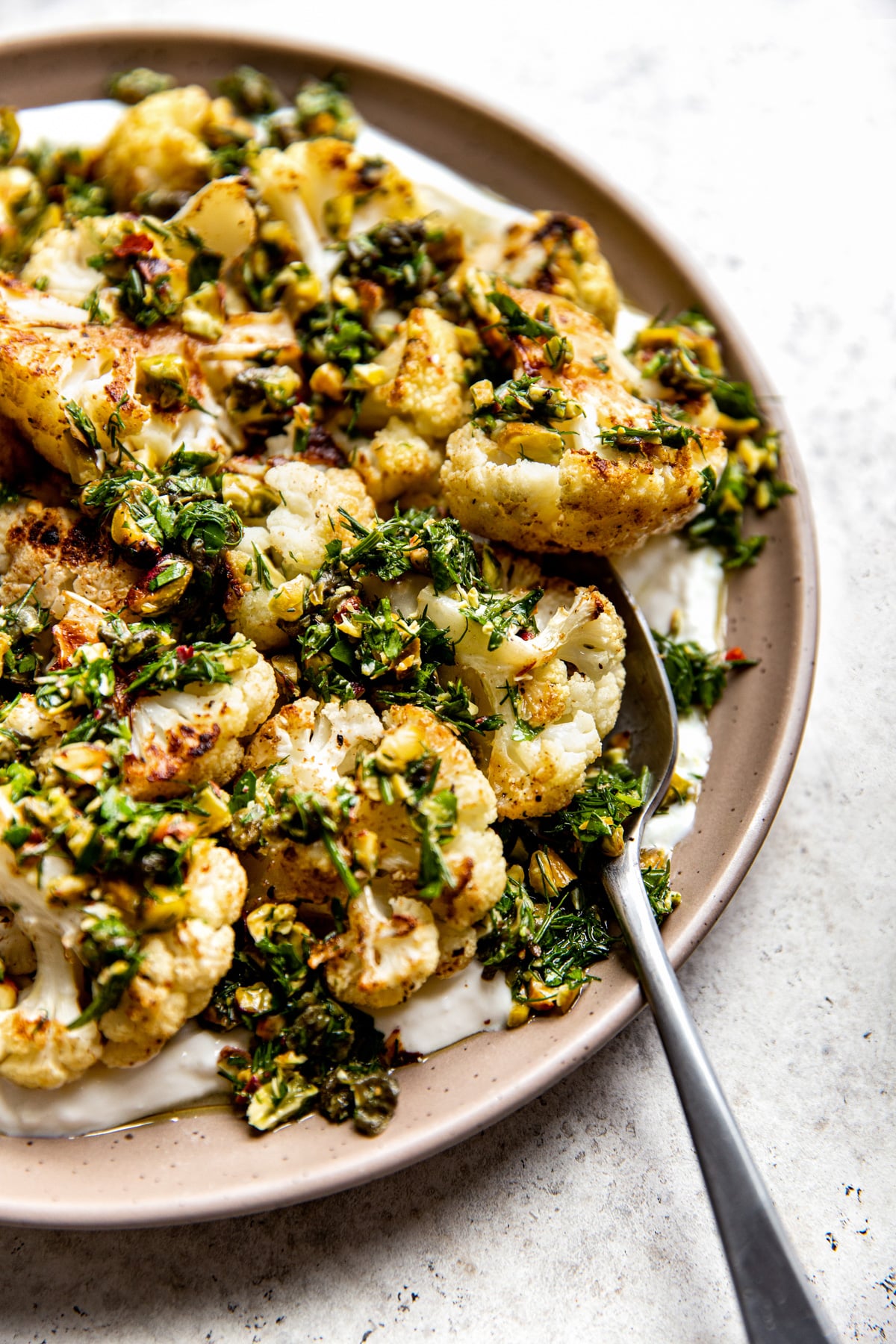 A serving spoon scooping up cauliflower, yogurt, and gremolata mixture.