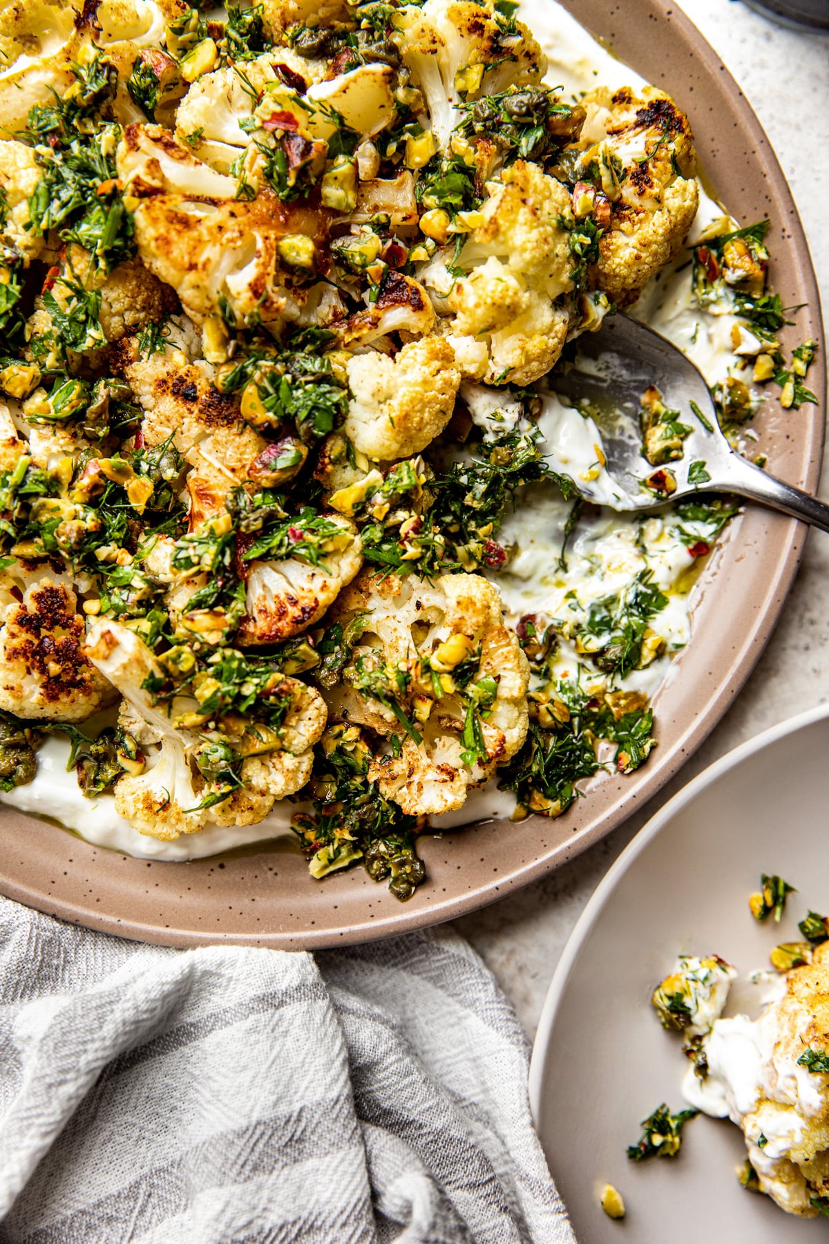 Roasted cauliflower florets being assembled over yogurt and topped with caper gremolata.