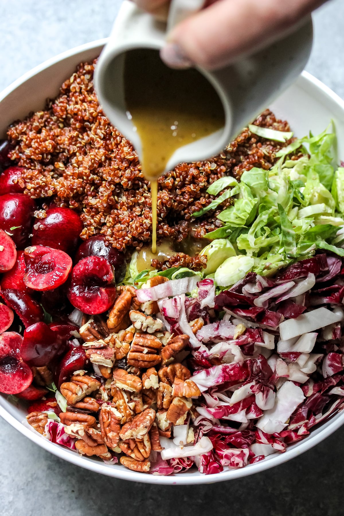 Maple-mustard dressing being poured over salad components in a large white mixing bowl.