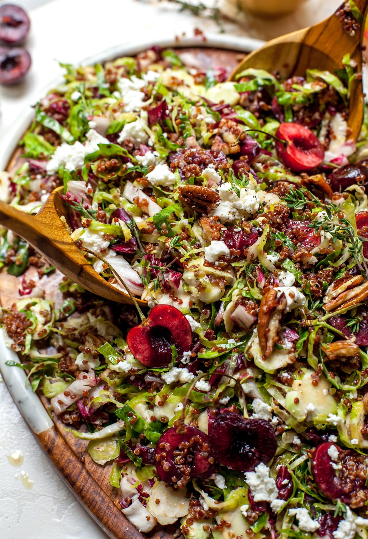 Cherry salad with Brussels, quinoa and goat cheese arranged on a wooden serving platter.