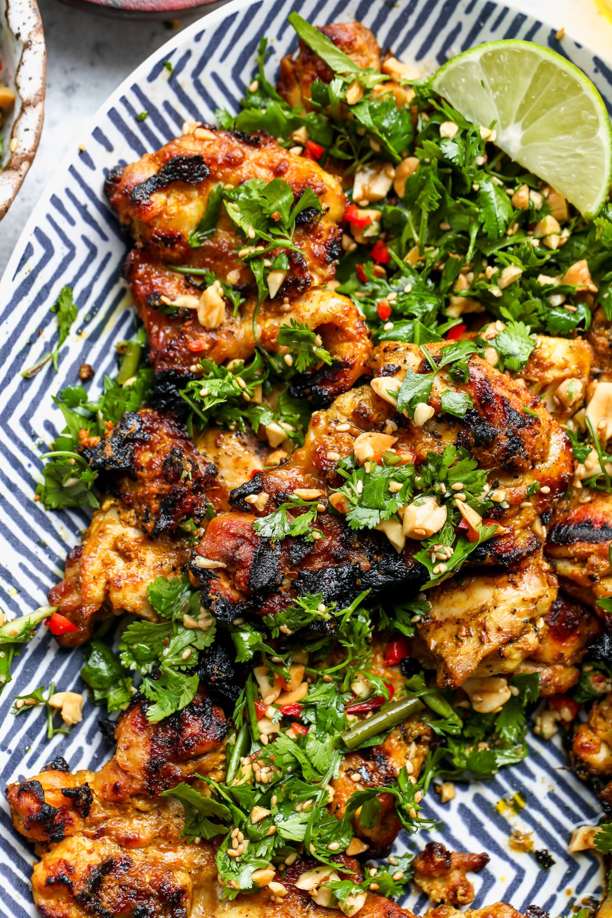 Curried chicken thighs arranged on a blue and white platter topped with cilantro and peanut mixture.