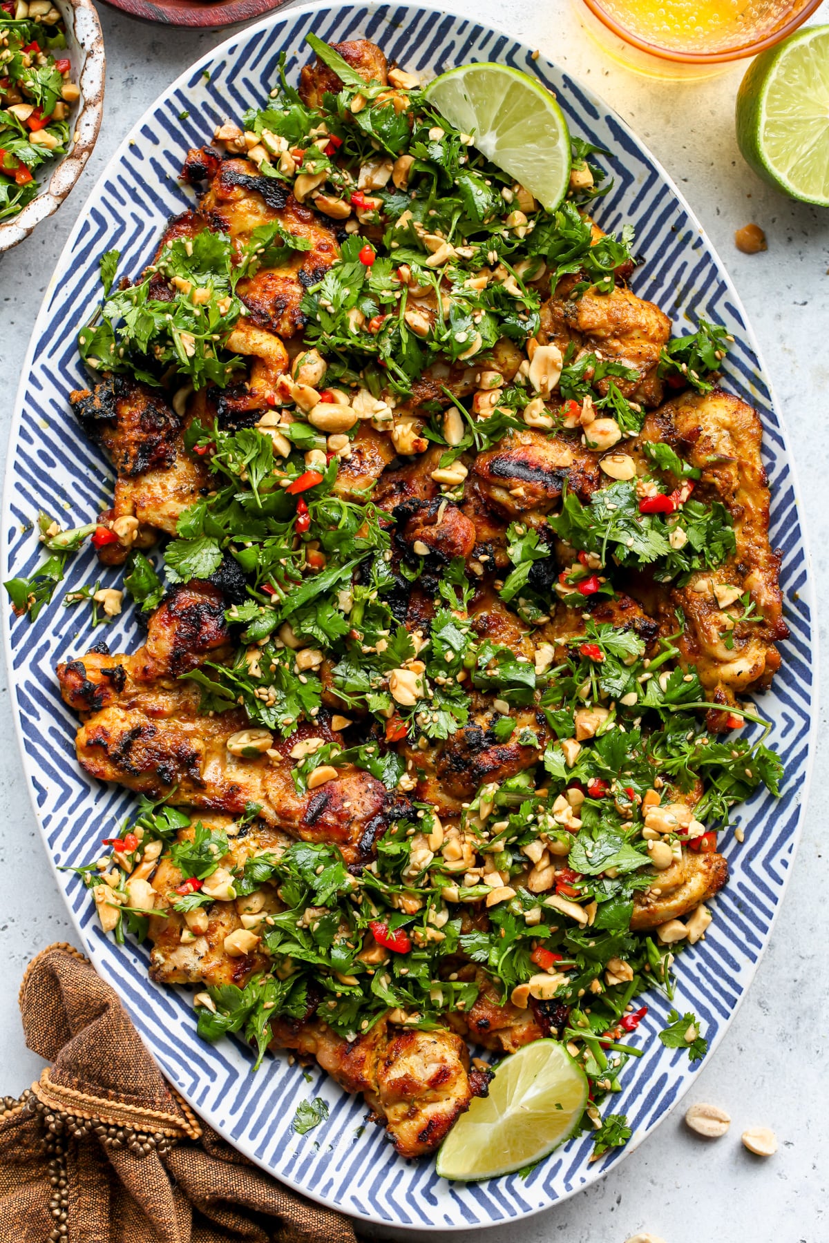 Curried chicken thighs topped with cilantro-peanut salad on a blue and white serving platter.