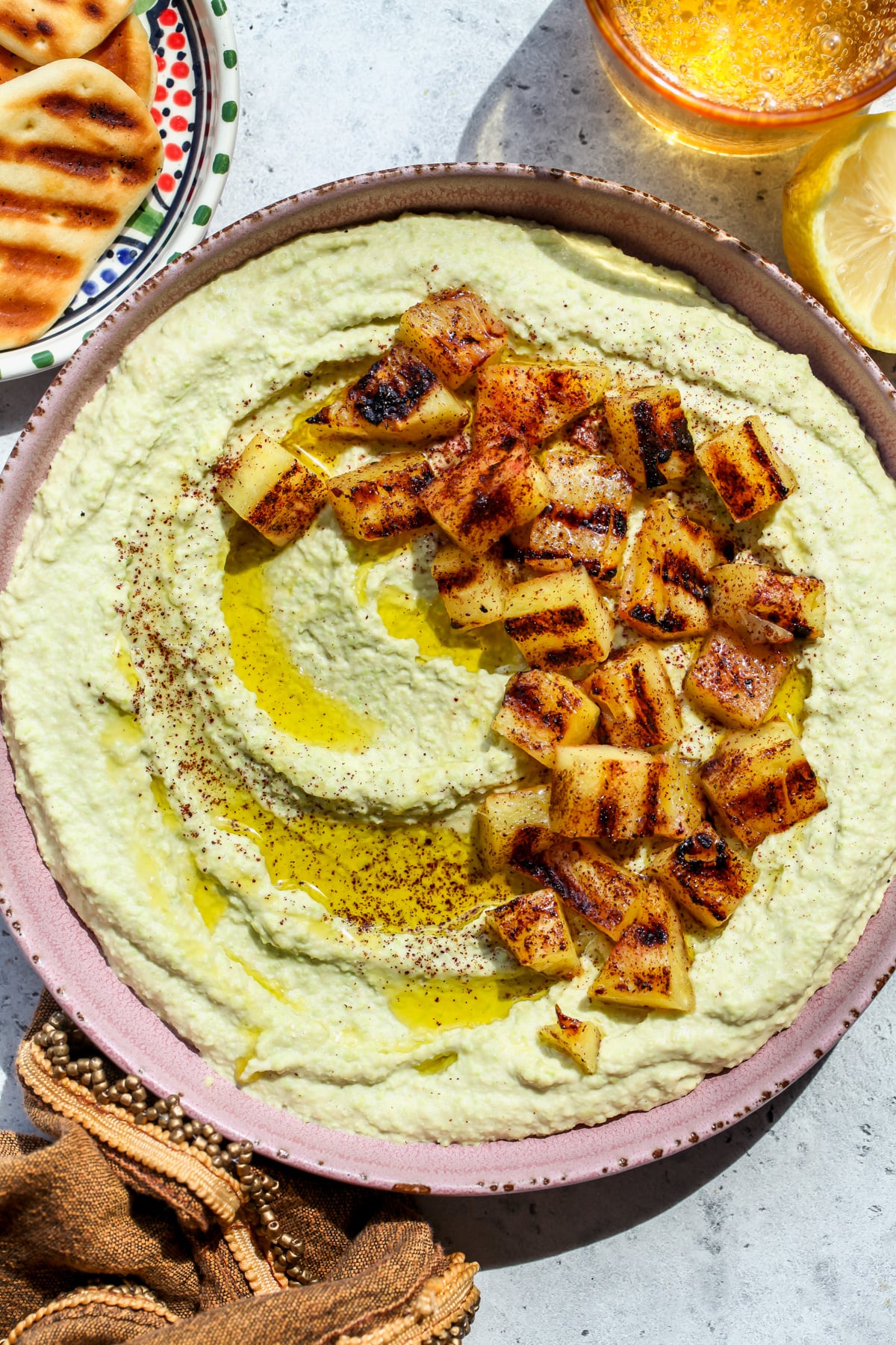 Edamame Hummus topped with chunks of sumac-grilled pineapple styled in a wide-rimmed pink bowl.