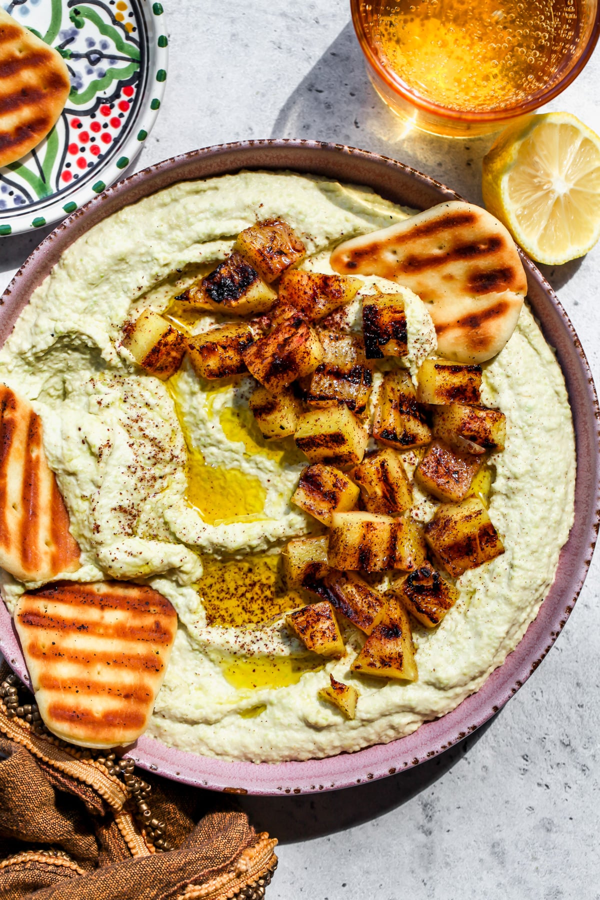 Edamame hummus topped with sumac grilled pineapple styled in a pink bowl.