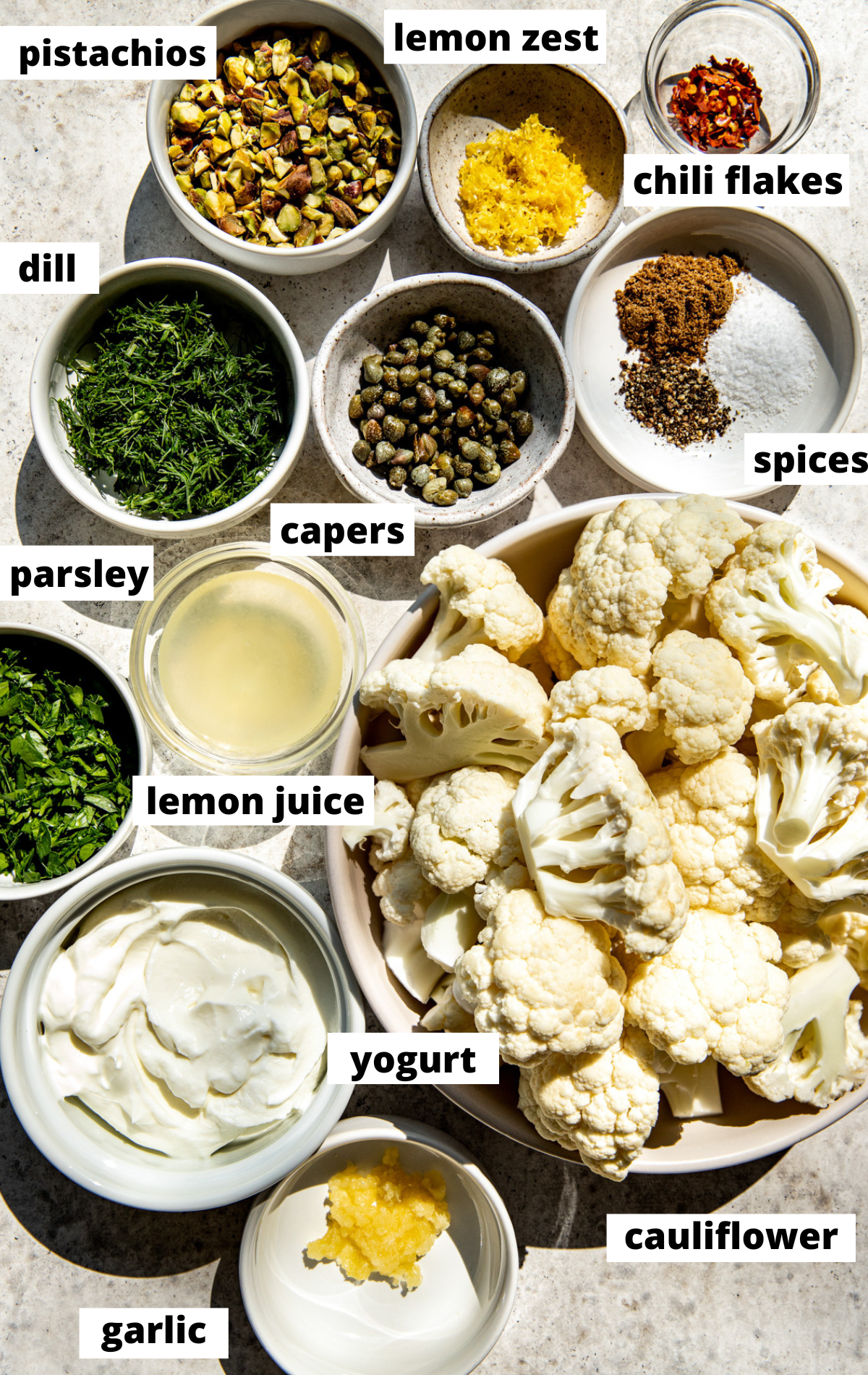 Recipe ingredients in separate bowls assembled on a white surface with labels.