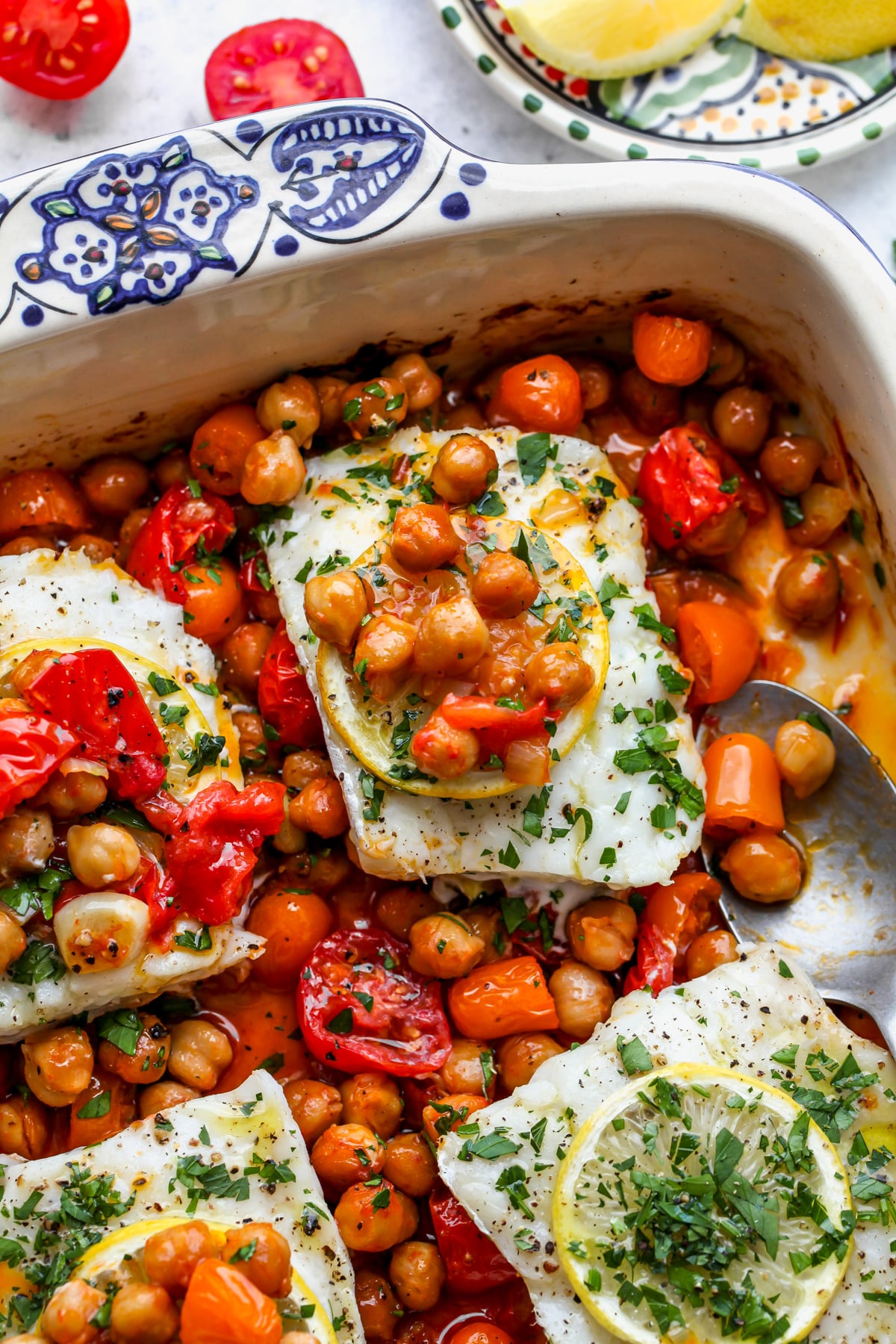 Moroccan baked fish topped with chickpeas and tomatoes in a blue and white baking dish.