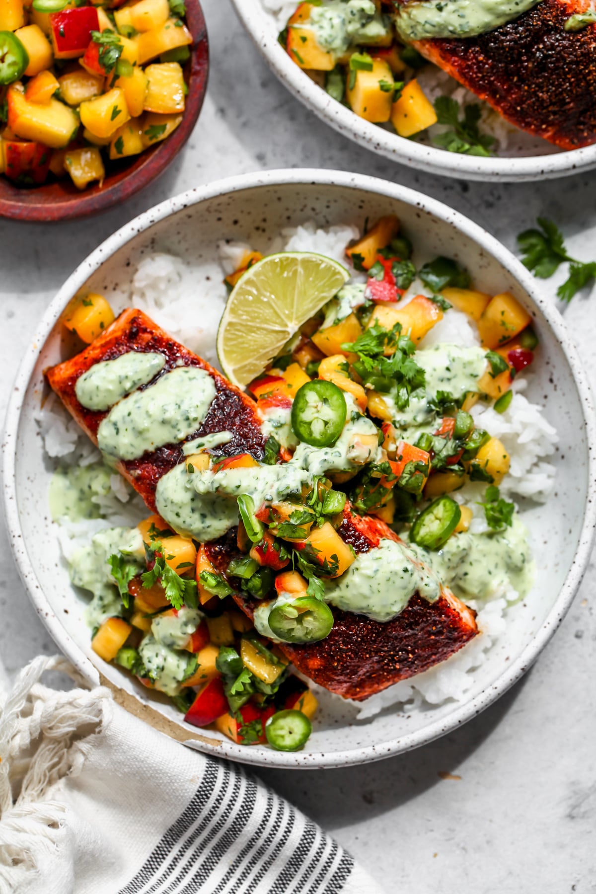 BBQ salmon bowls in a white bowl topped with peach salsa and cilantro sauce.