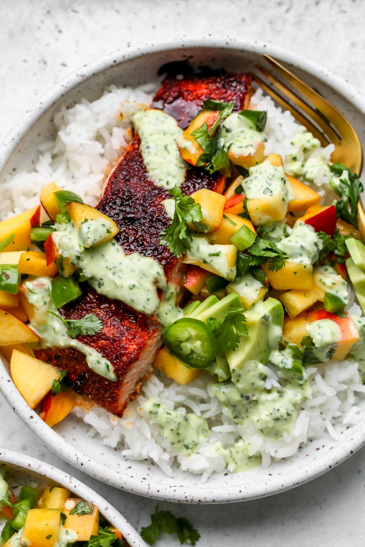 A fully assembled BBQ salmon bowl including one salmon fillet, rice, peach salsa, and cilantro sauce.