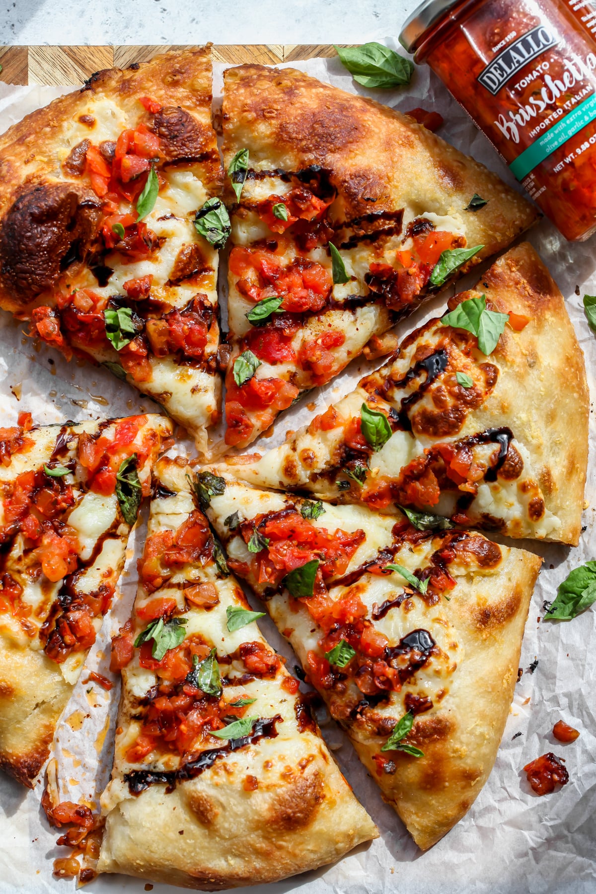 A jar of DeLallo Bruschetta laying next to a sliced Bruschetta Pizza.