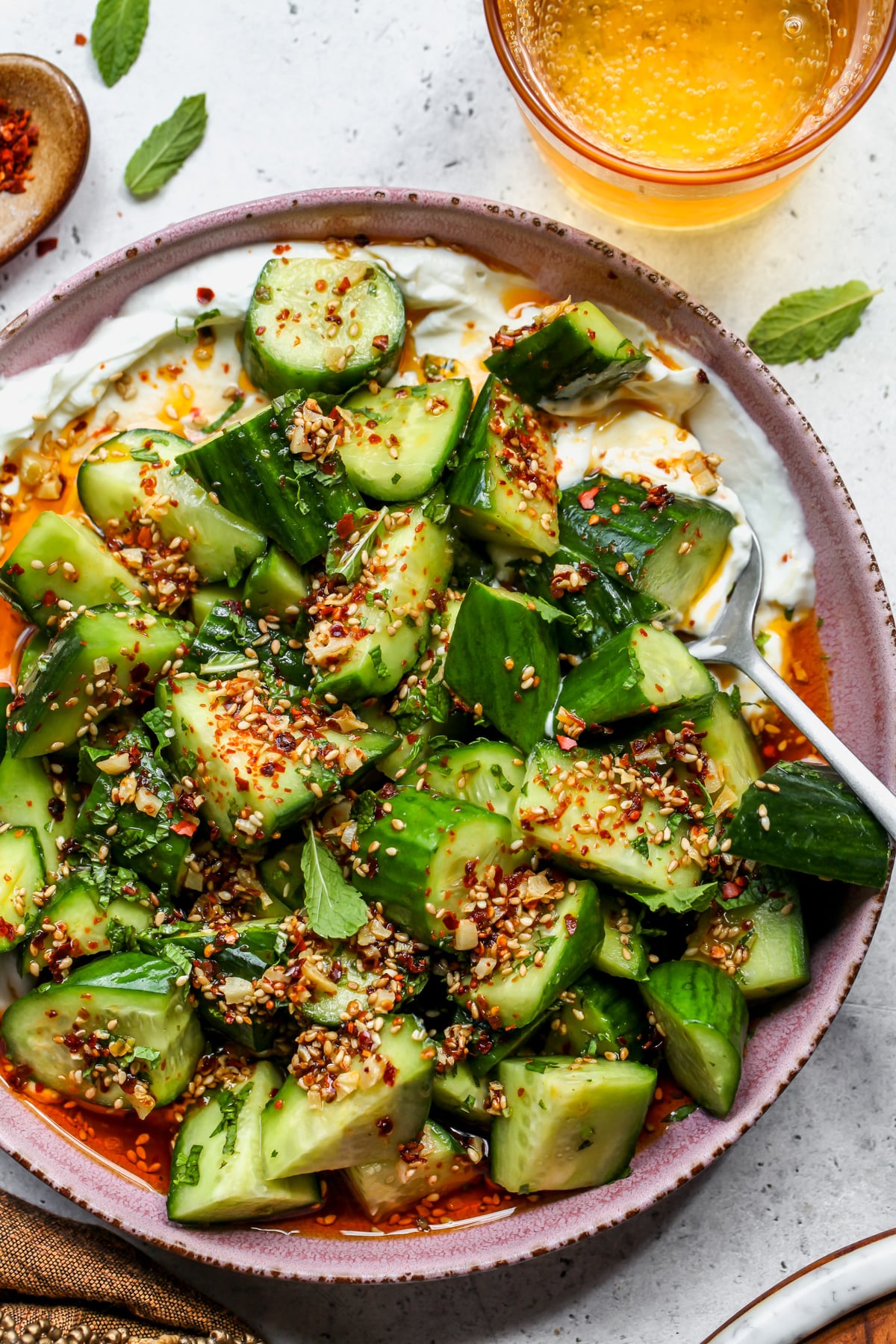 A spoon scooping a portion of yogurt and cucumber salad out of a pink bowl.