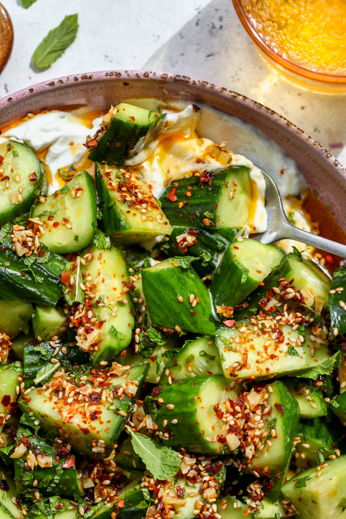 A close up of cucumber sesame salad in a pink bowl topped with chili oil.