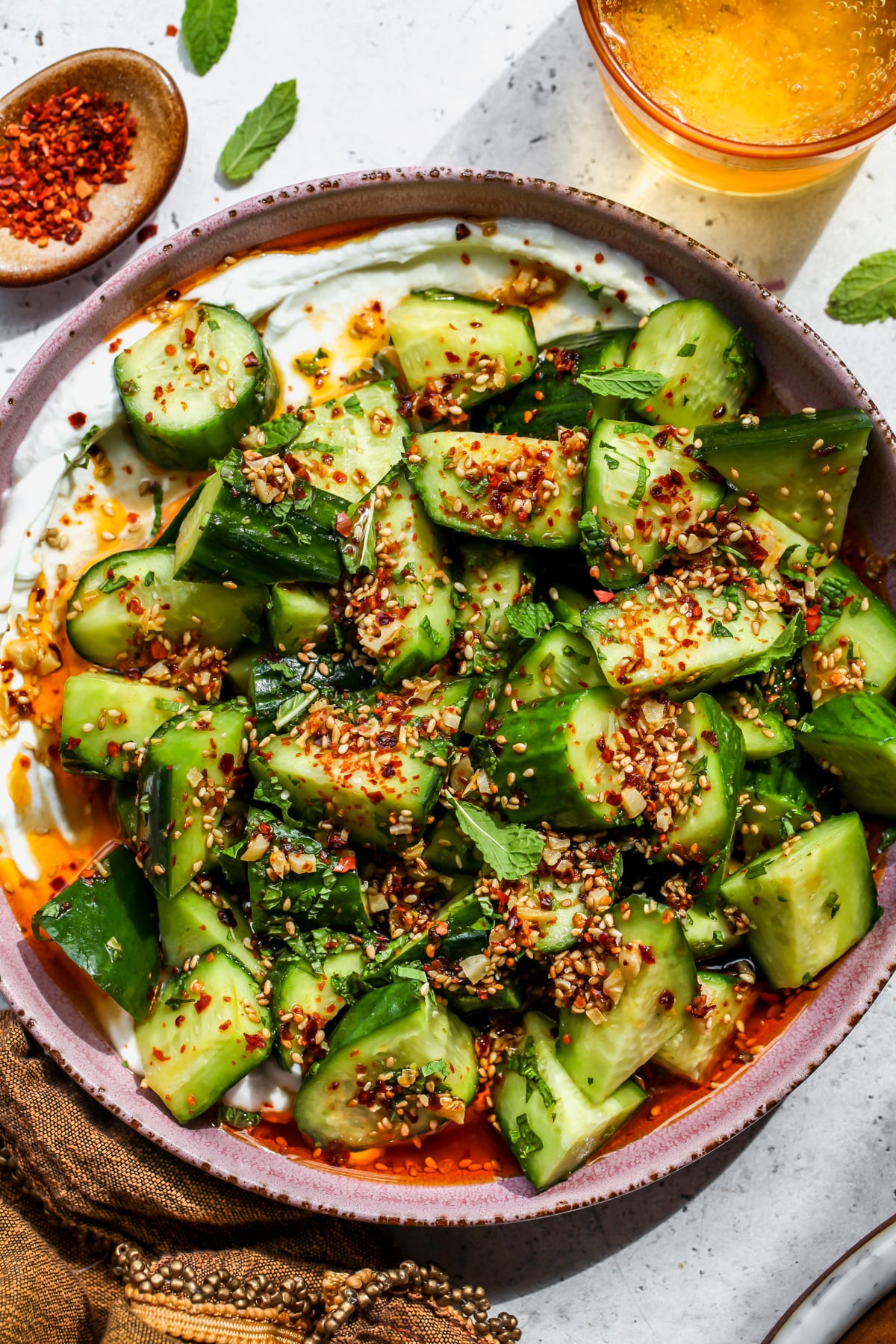 Cucumber sesame salad topped with garlicky chili oil served over yogurt in a pink bowl.