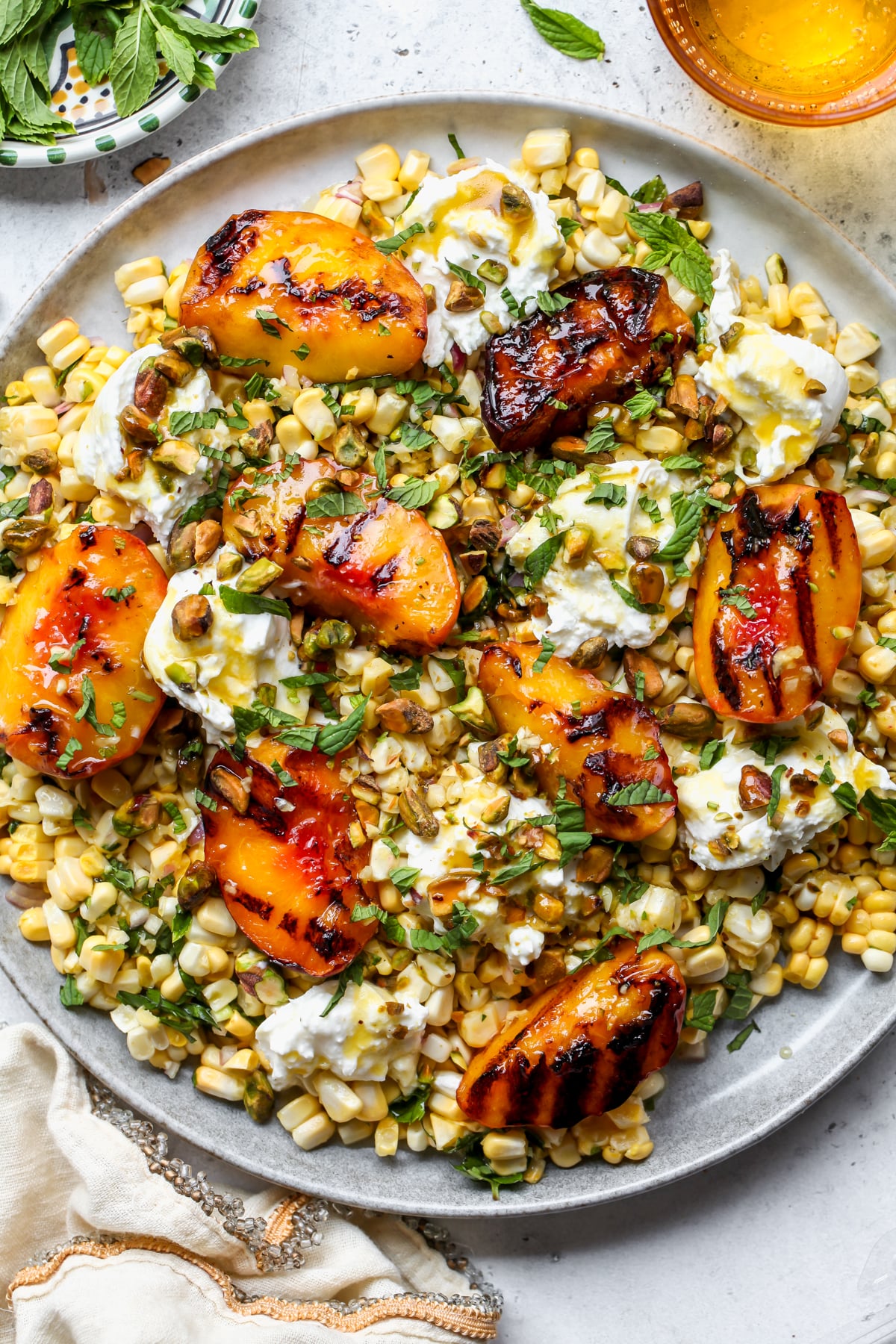 Peach Burrata Salad topped with herbs, pistachios, and hot honey dressing styled on a gray platter.