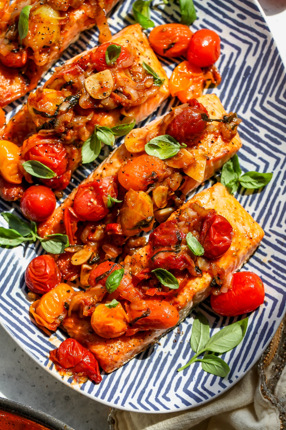 Salmon with balsamic tomatoes on a platter topped with fresh basil leaves.