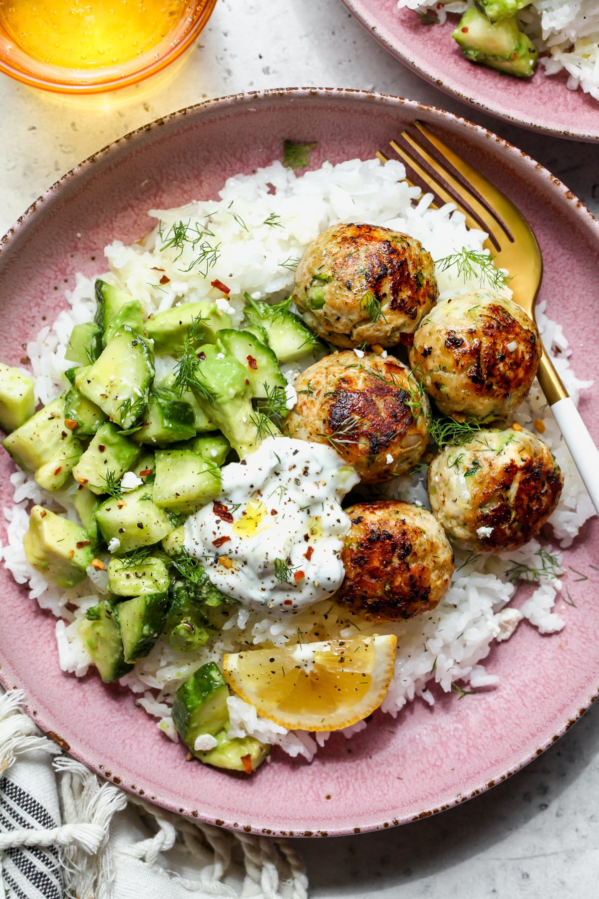 Chicken zucchini meatballs styled in a pink bowl over rice with cucumber-avocado salad.