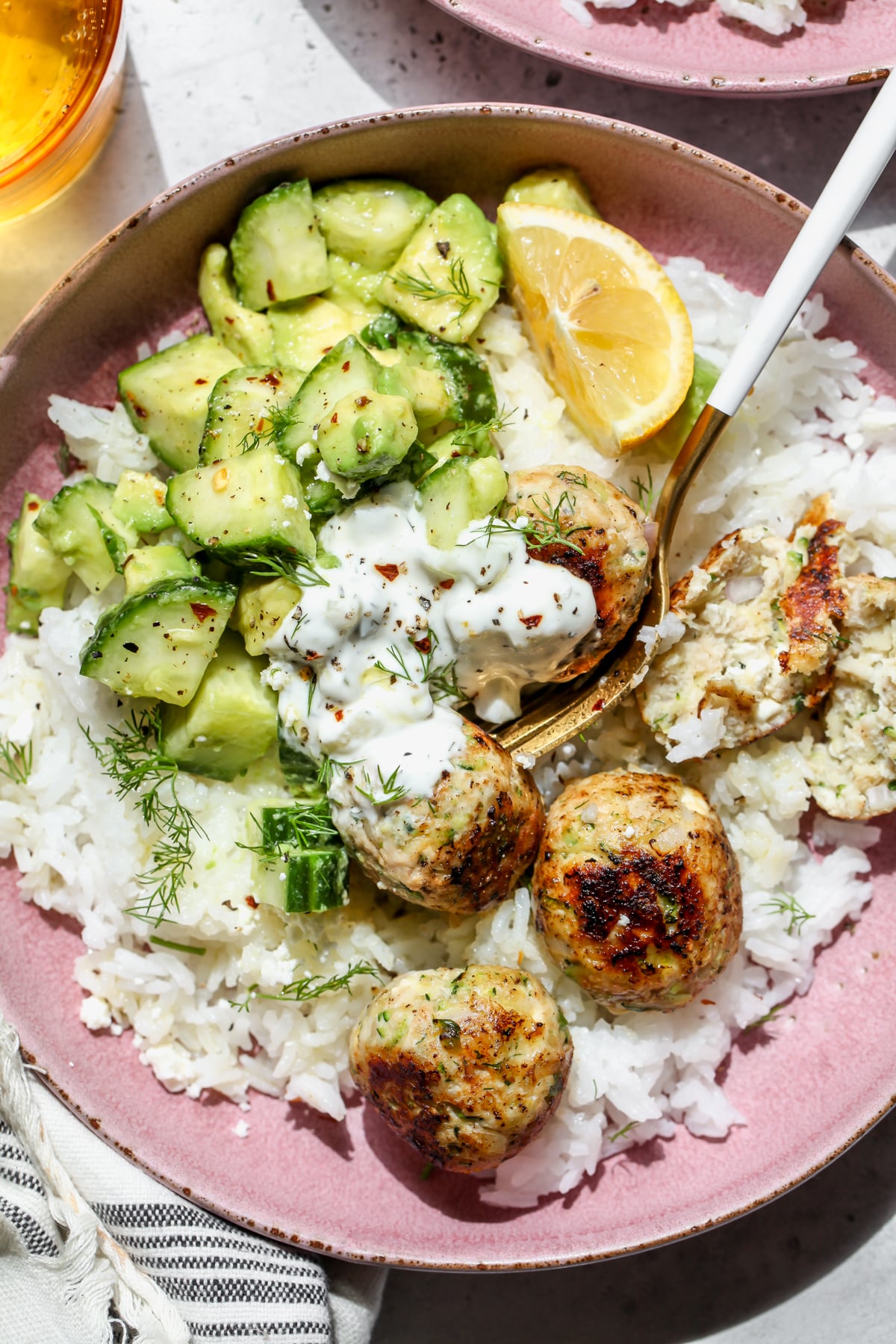 Chicken zucchini meatballs served over rice with tzatziki and cucumber salad in a pink bowl.