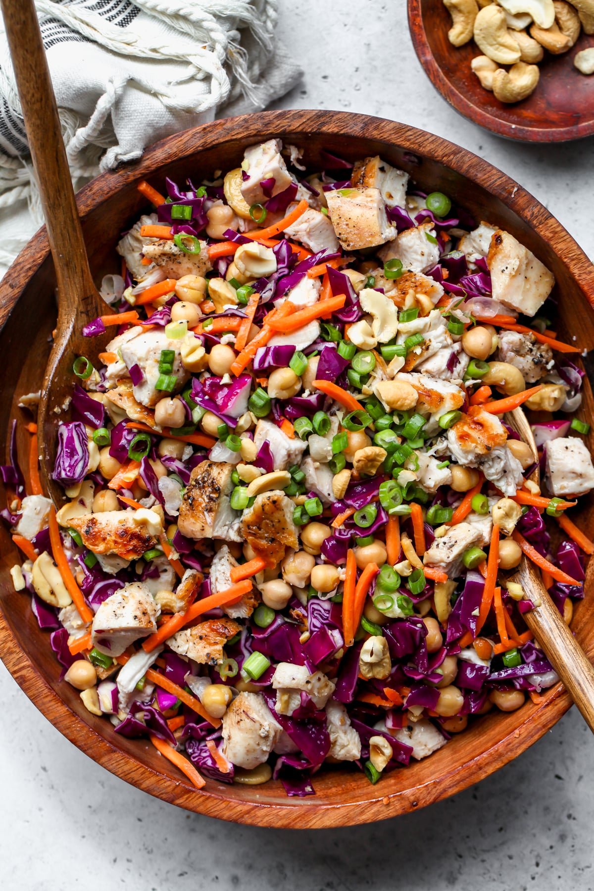 A wooden serving bowl filled with Sesame chicken and chickpea salad. Salad tongs resting on each side.